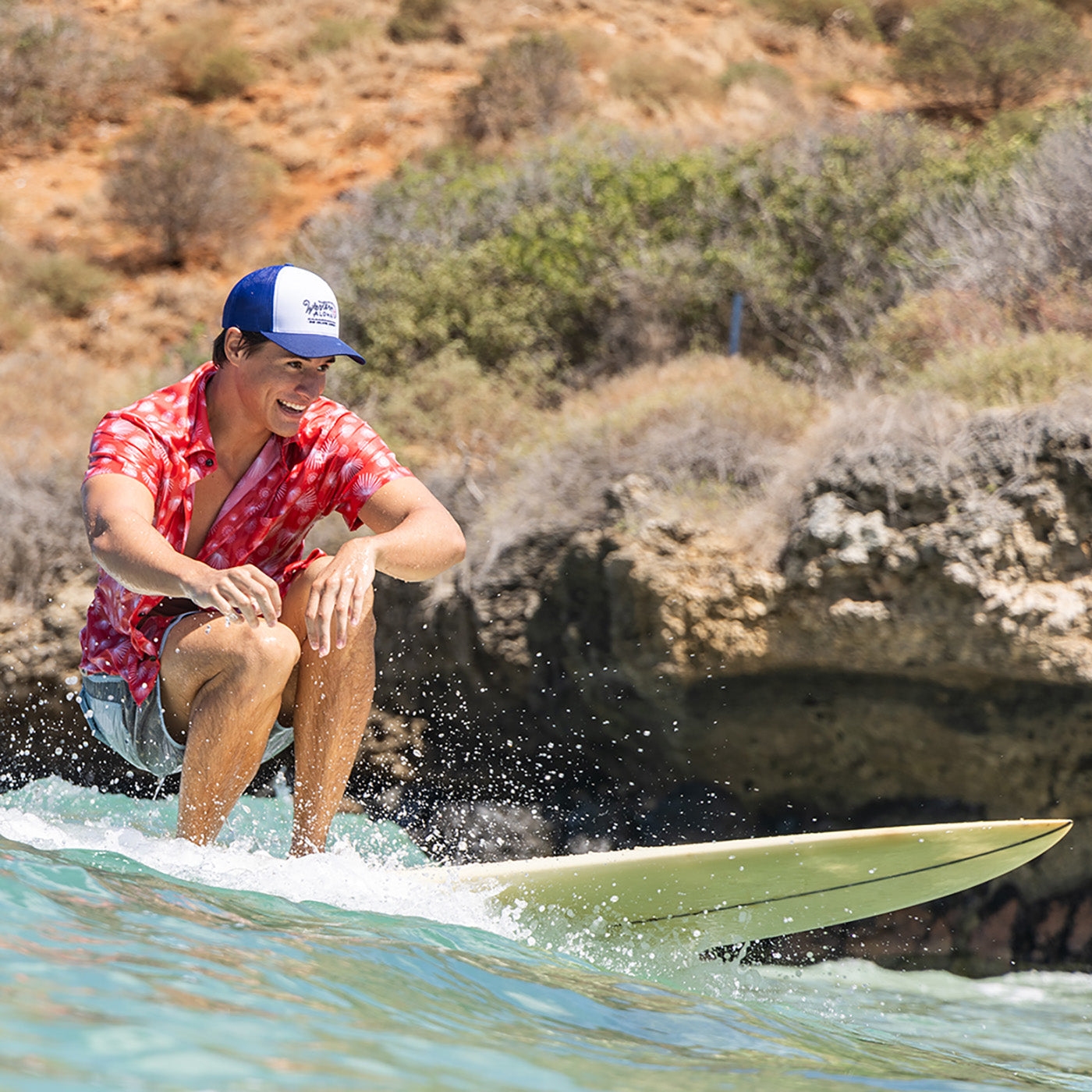 Person surfing with a scenic background of rocks and water.