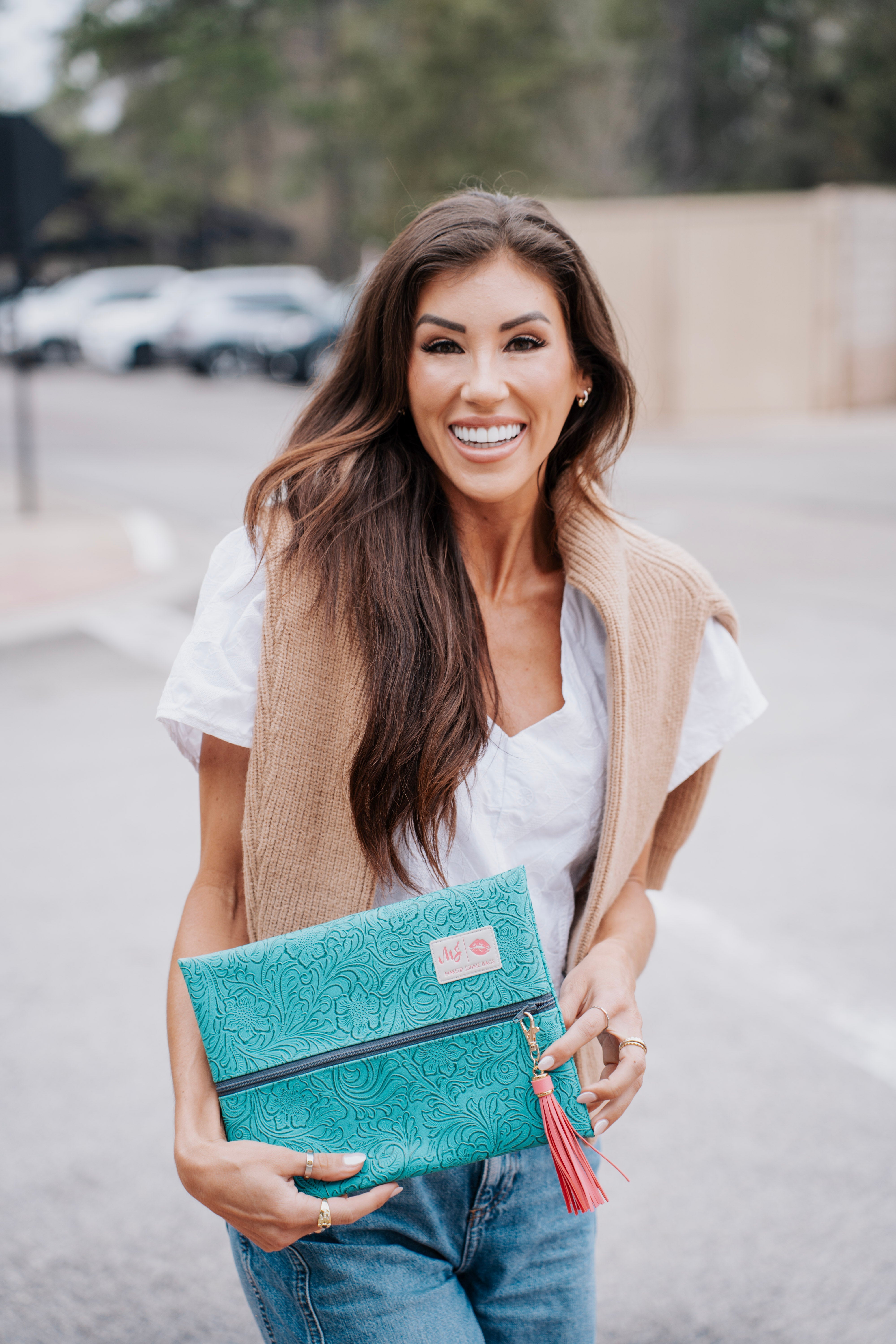 Woman holding a turquoise clutch with a tassel in an outdoor setting