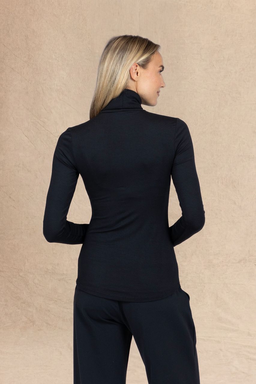 A woman shown from the back wearing a fitted black long-sleeve mock neck top and matching black pants against a textured beige studio backdrop.