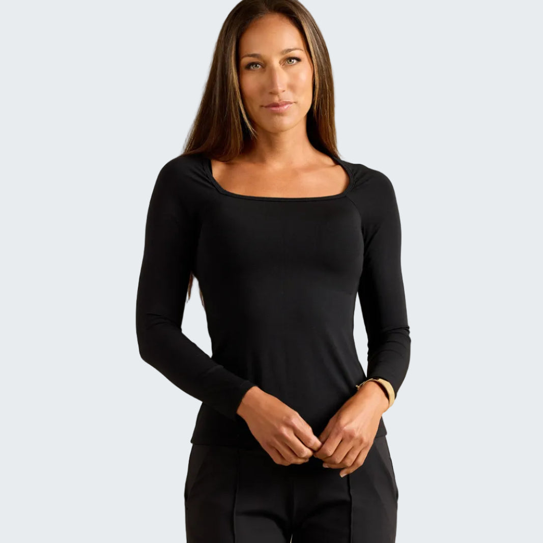 A woman modeling a black long-sleeve scoop-neck top and black pants against a textured beige studio background.