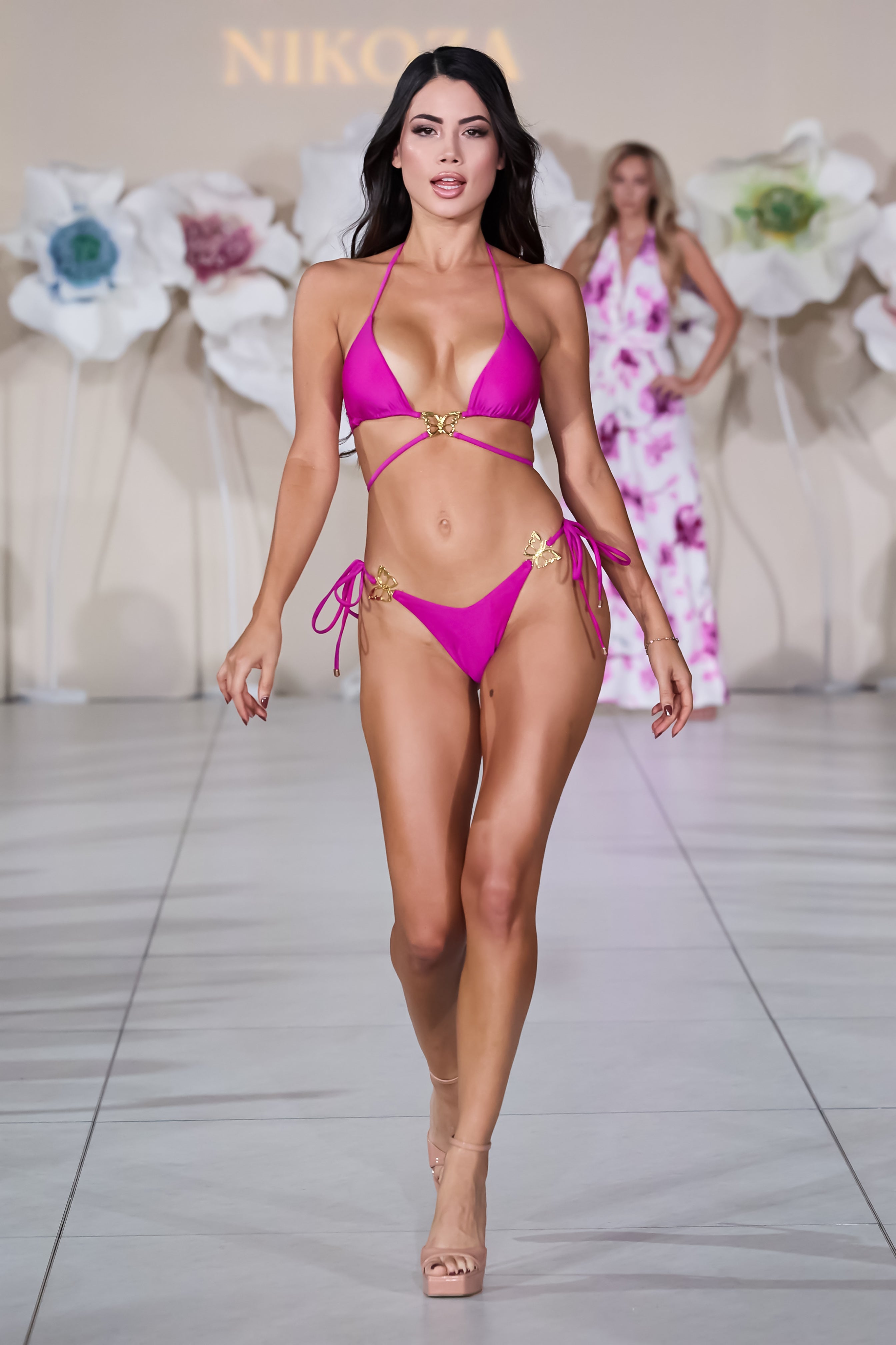 Model wearing a pink bikini walking on a runway with 'Nikolai' branding.