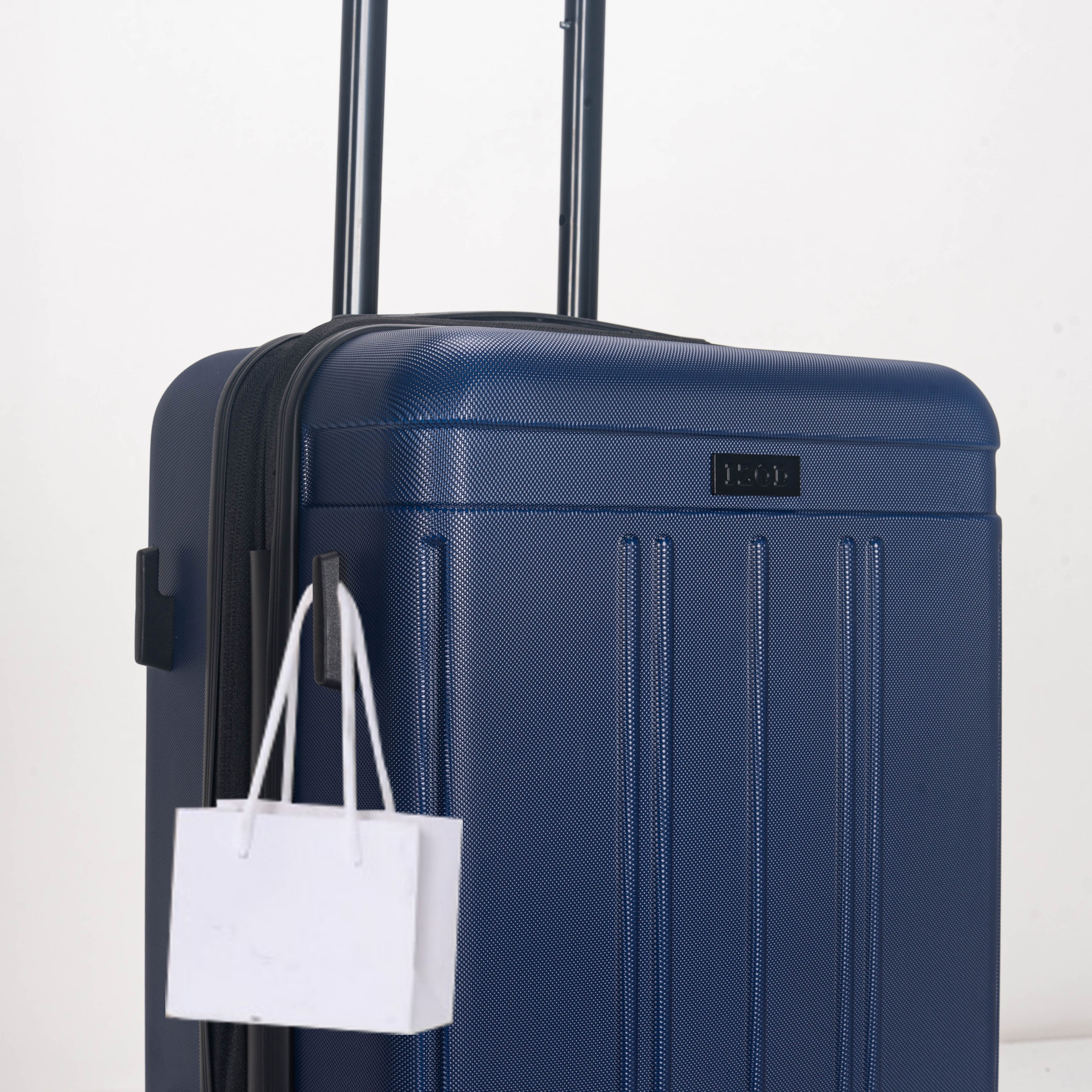 Blue suitcase with a white shopping bag attached on a light gray background