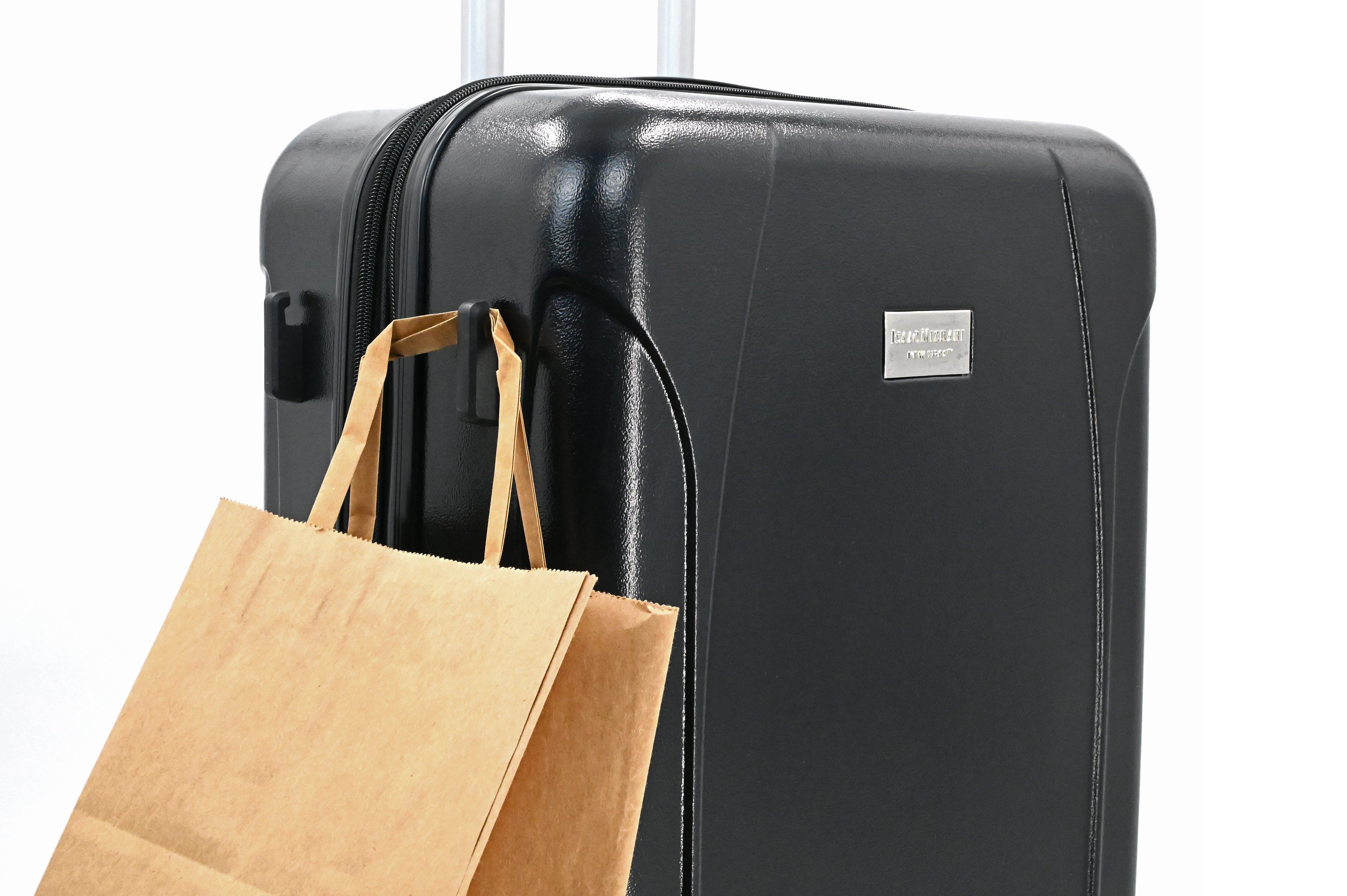 Black suitcase with a brown paper bag attached to it on a white background