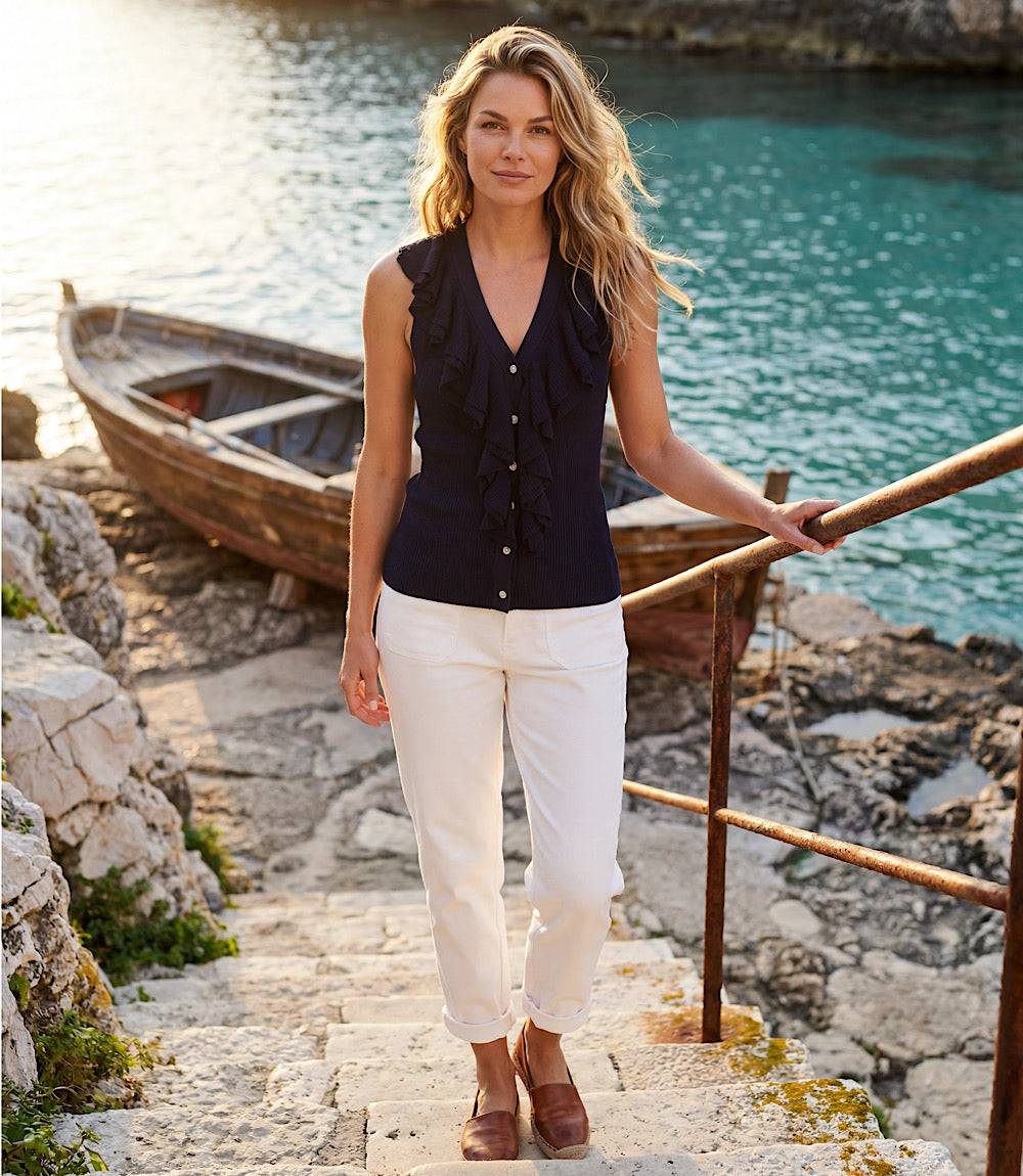 Woman standing on stone steps by a body of water with a boat in the background