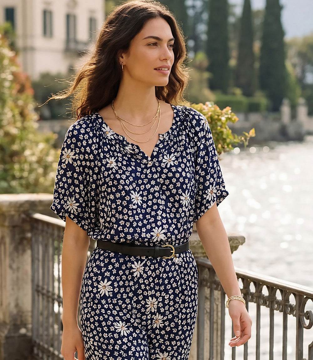 Woman wearing a navy floral dress standing by a waterfront with greenery.