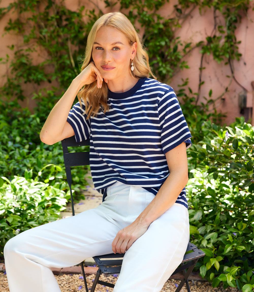 Woman wearing a navy and white striped shirt sitting outdoors with greenery in the background