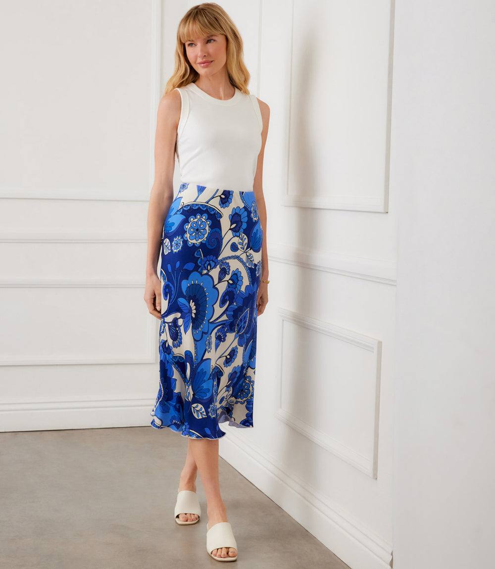 Woman wearing a white sleeveless top and blue floral skirt against a white wall.