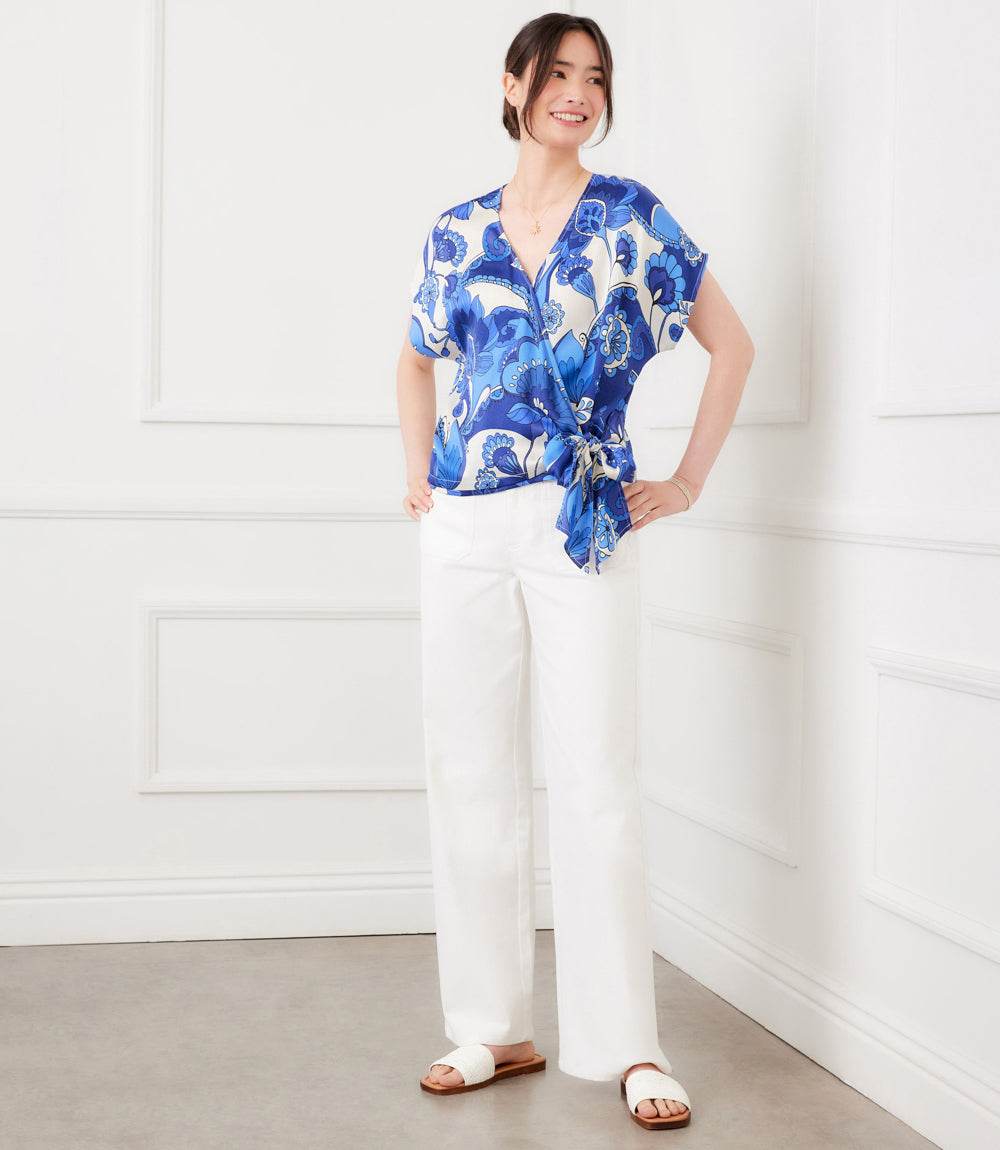 Woman wearing a blue floral top and white pants in a minimalistic room.