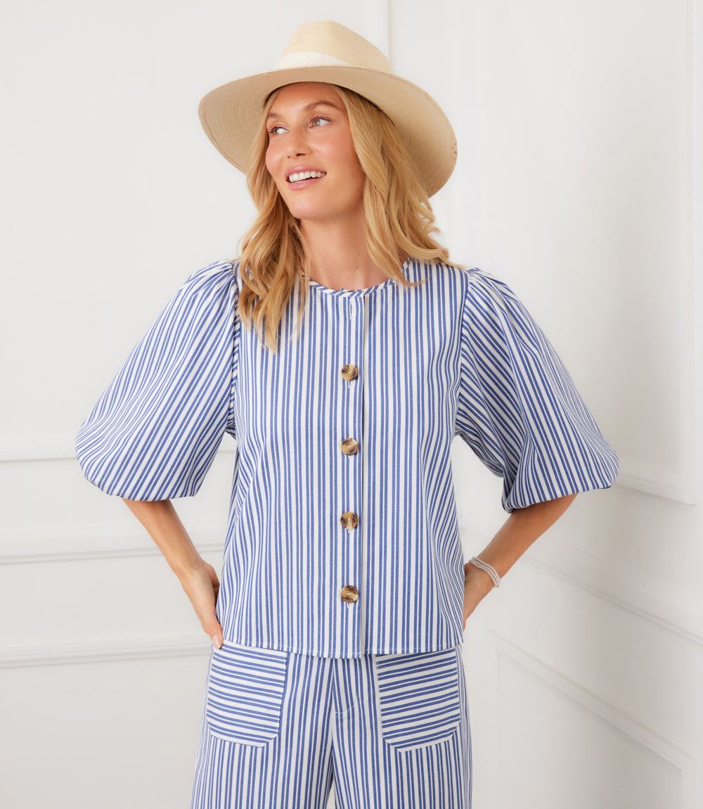 Woman wearing a blue and white striped outfit with a beige hat against a white background