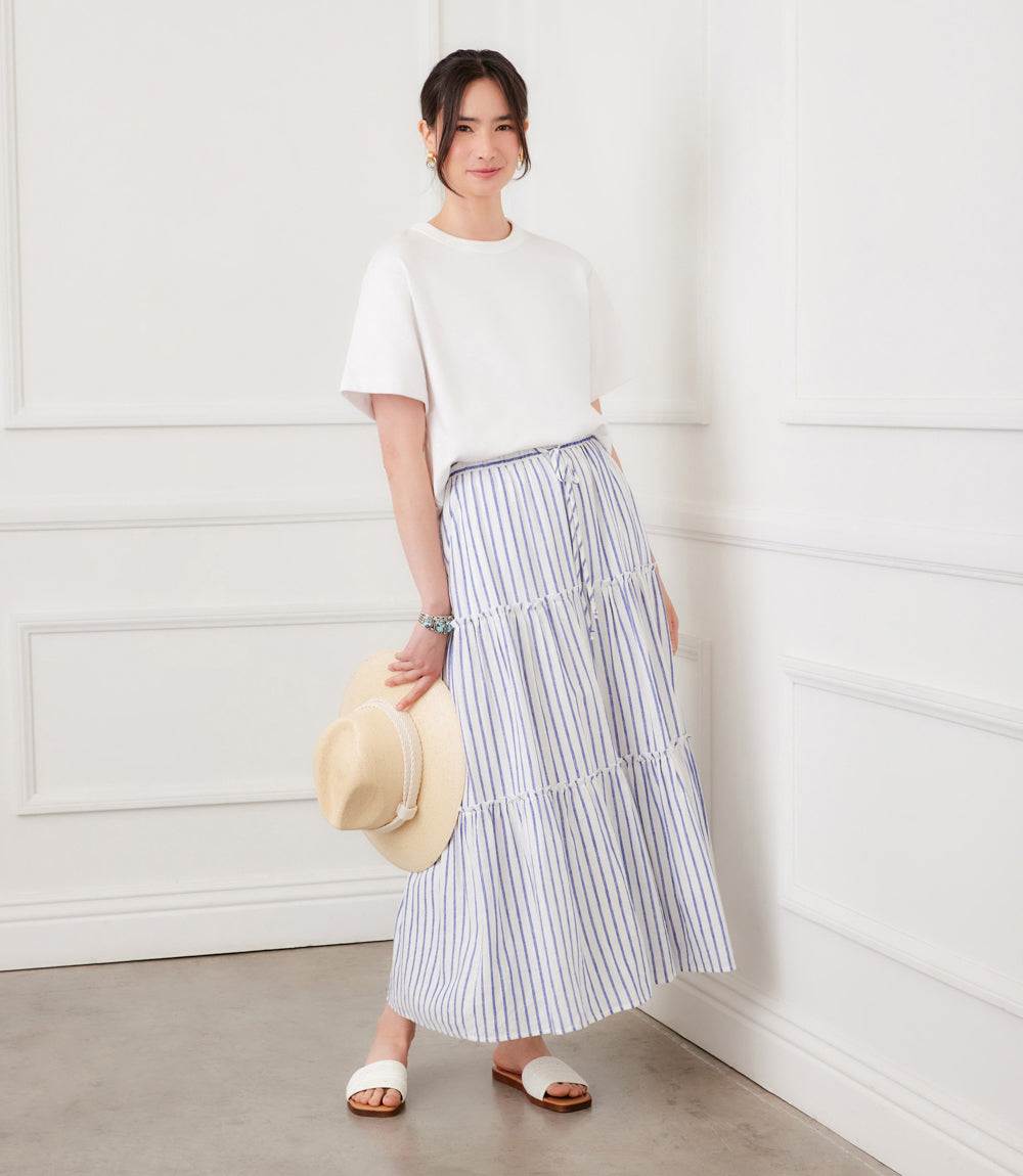 Woman wearing a white top and striped skirt, holding a hat indoors.