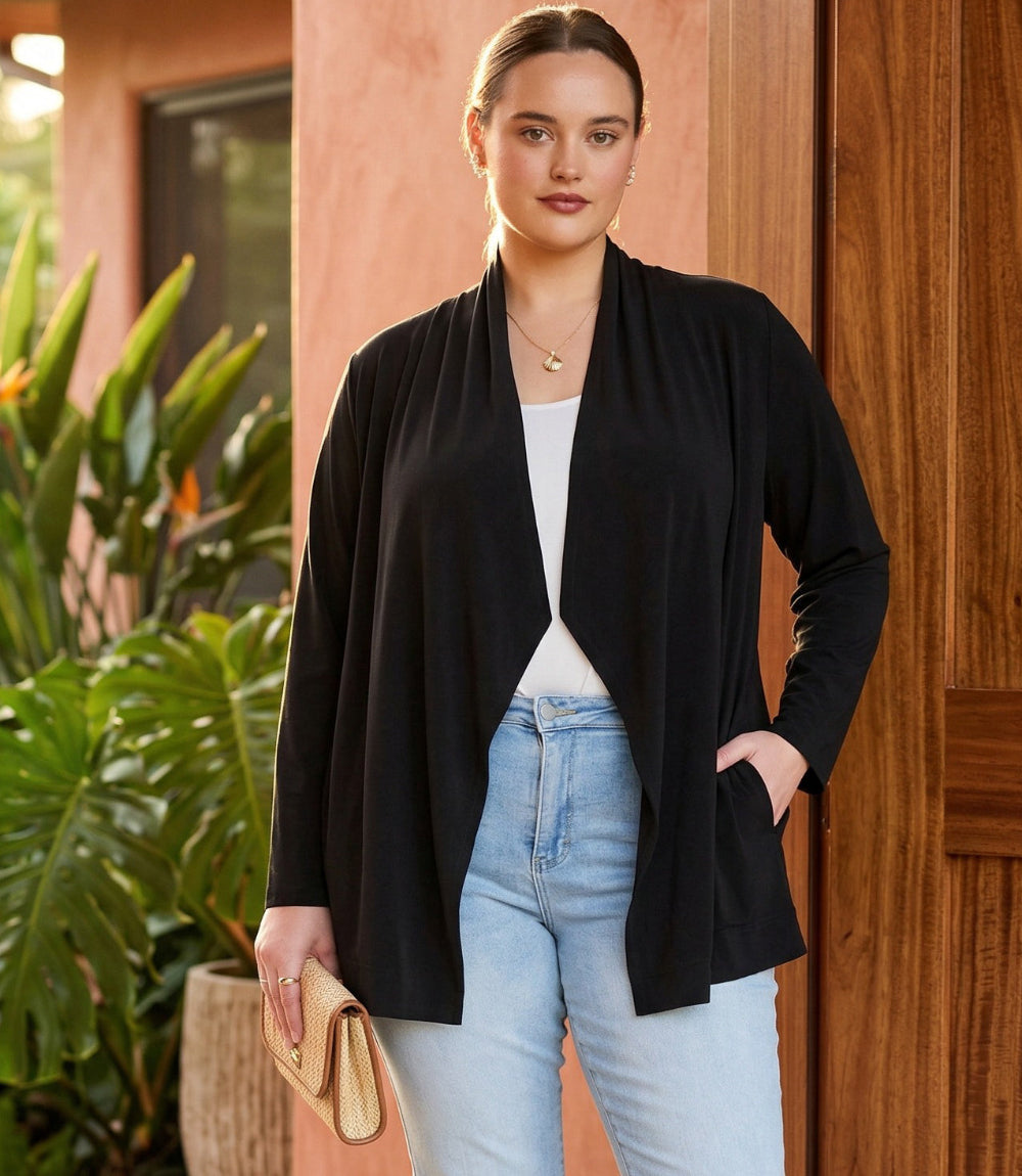 Woman wearing a black cardigan over a white top and light blue jeans, standing in front of a wooden door.