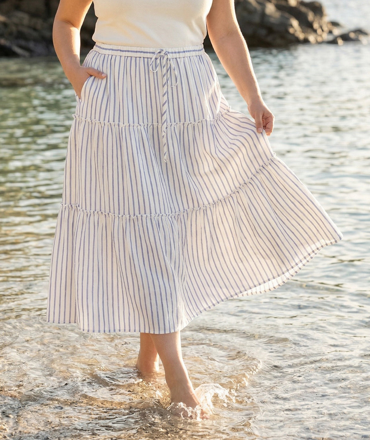 Person wearing a striped skirt standing in water near rocks