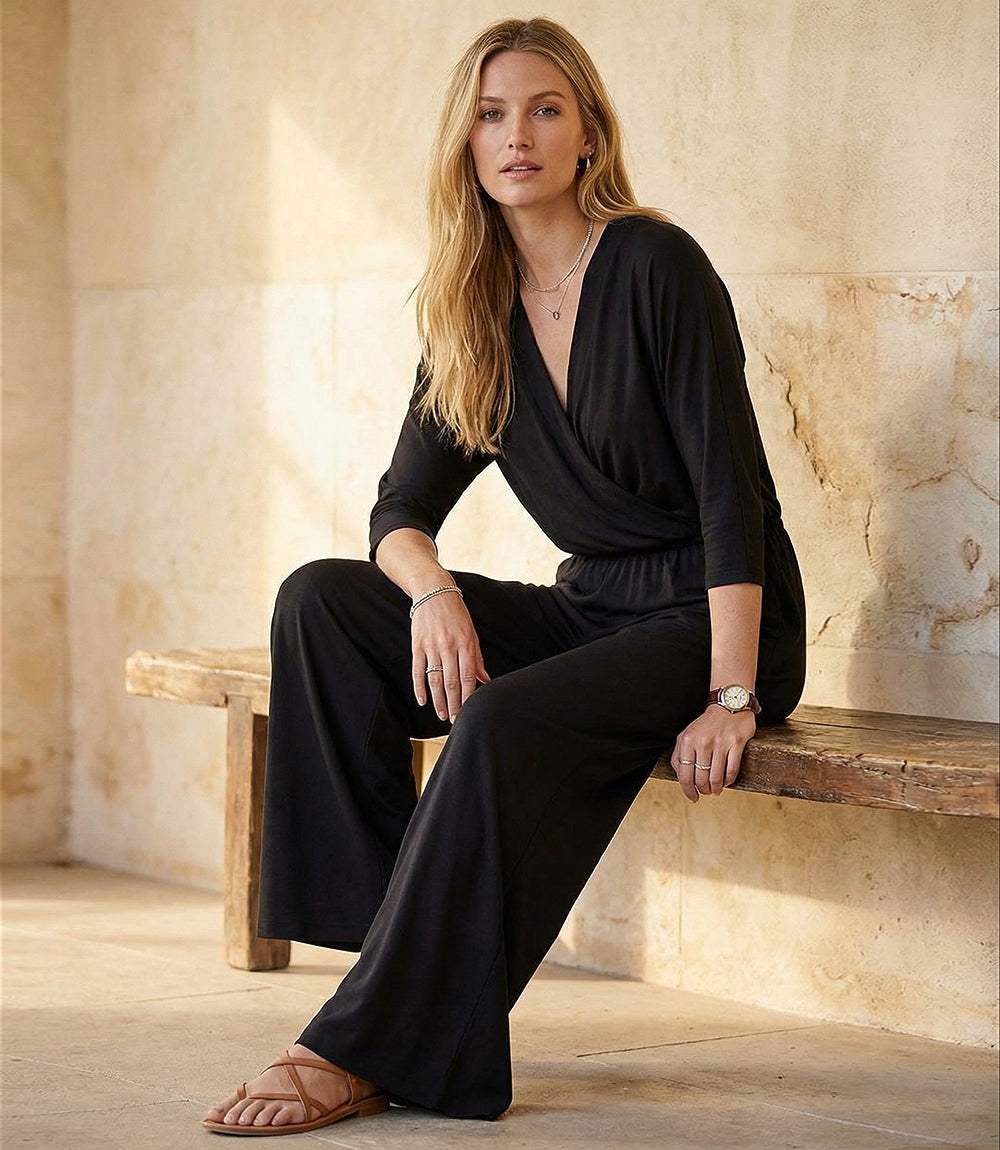 Woman in a black outfit sitting on a wooden bench against a textured wall.