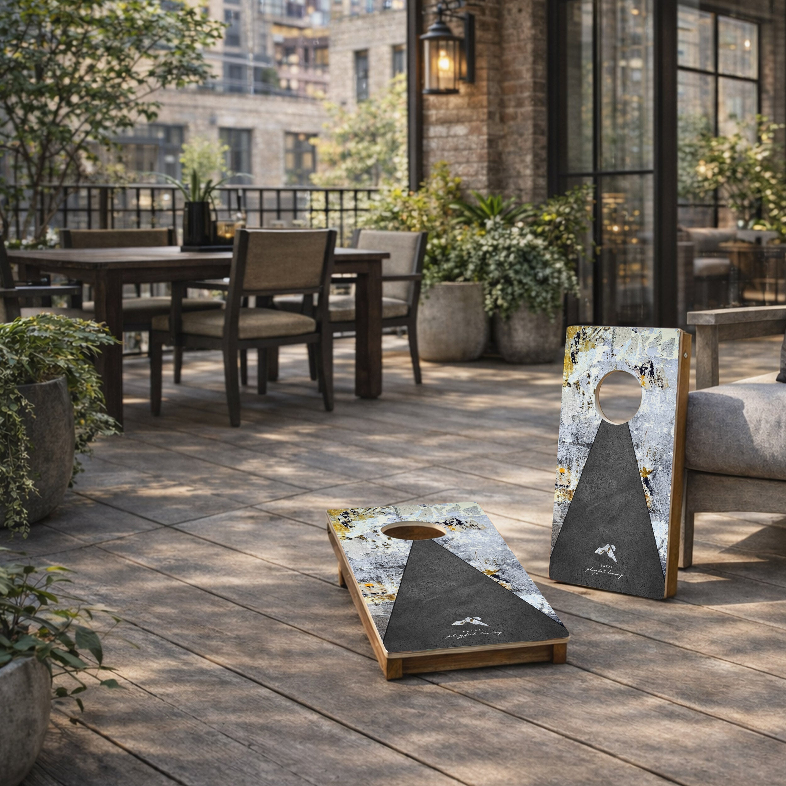 Cornhole boards on a wooden patio with outdoor furniture and plants in the background