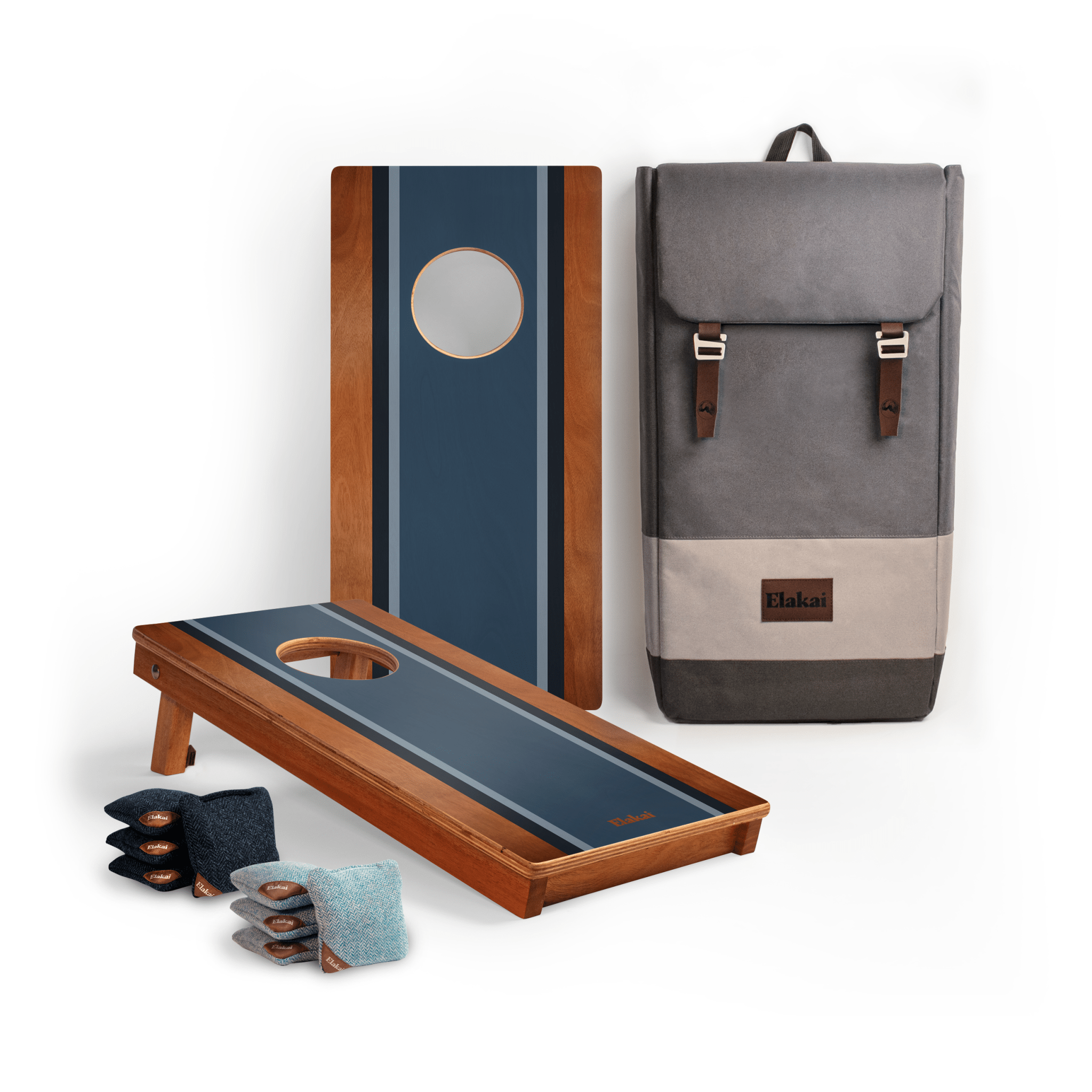 A cornhole set displayed on a white background, including two wooden boards with blue striped playing surfaces, a gray backpack-style carrying case with brown leather straps, and several bean bags in blue, gray, and black.