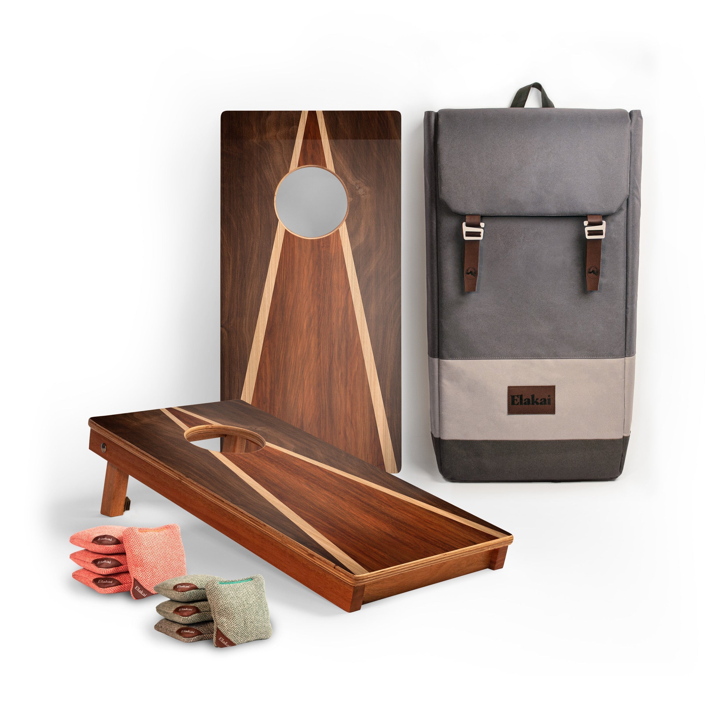 A wooden cornhole set displayed on a white background, including two wooden boards with geometric inlay patterns, a gray fabric carrying backpack, and several bean bags in pink, gray, and green. A small brown leather patch on the backpack shows the brand name 'Hakko'.