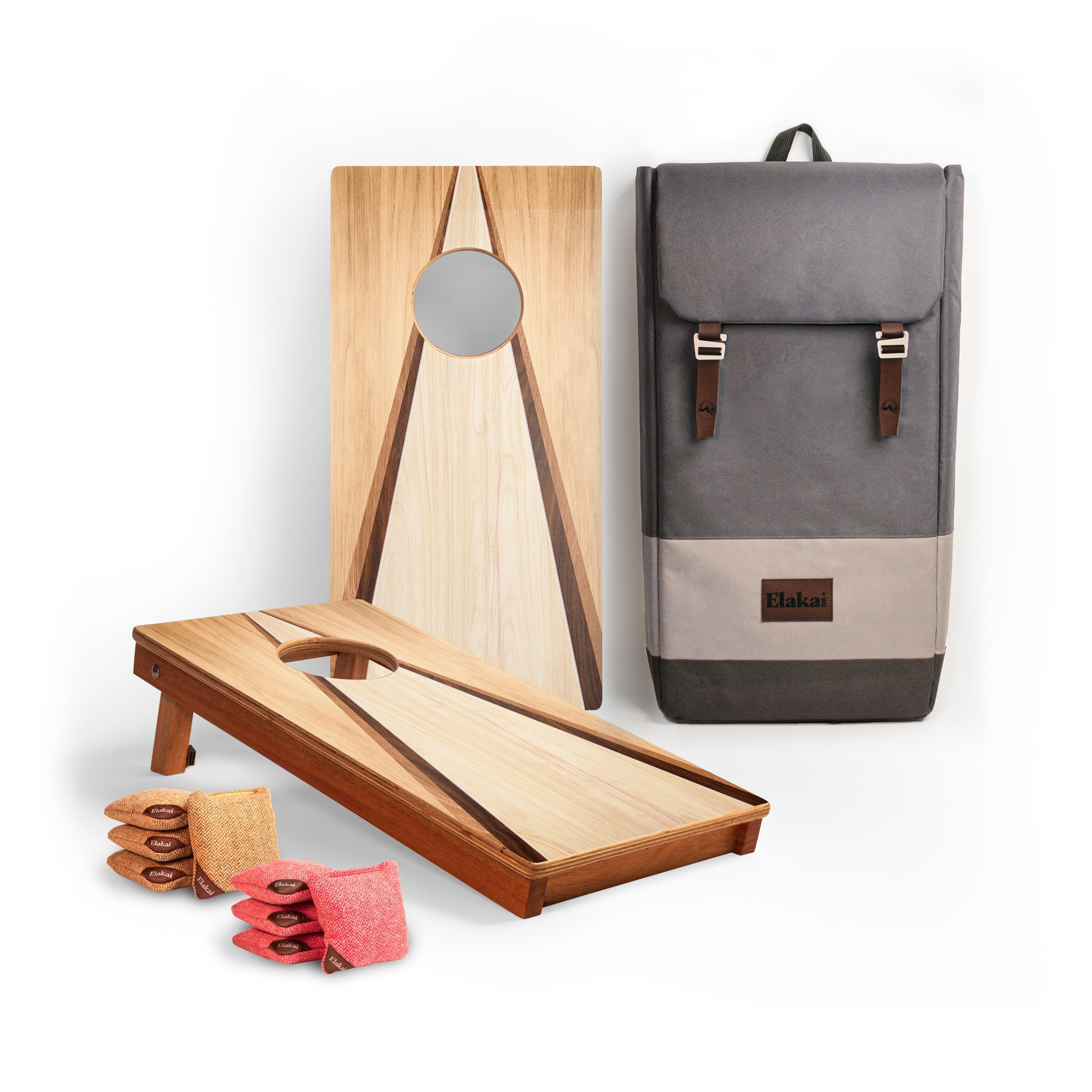 A cornhole set displayed on a white background, including two wooden boards, a gray and beige backpack, and pink bean bags. A small brown leather patch on the backpack shows the brand name 'Hakui'.