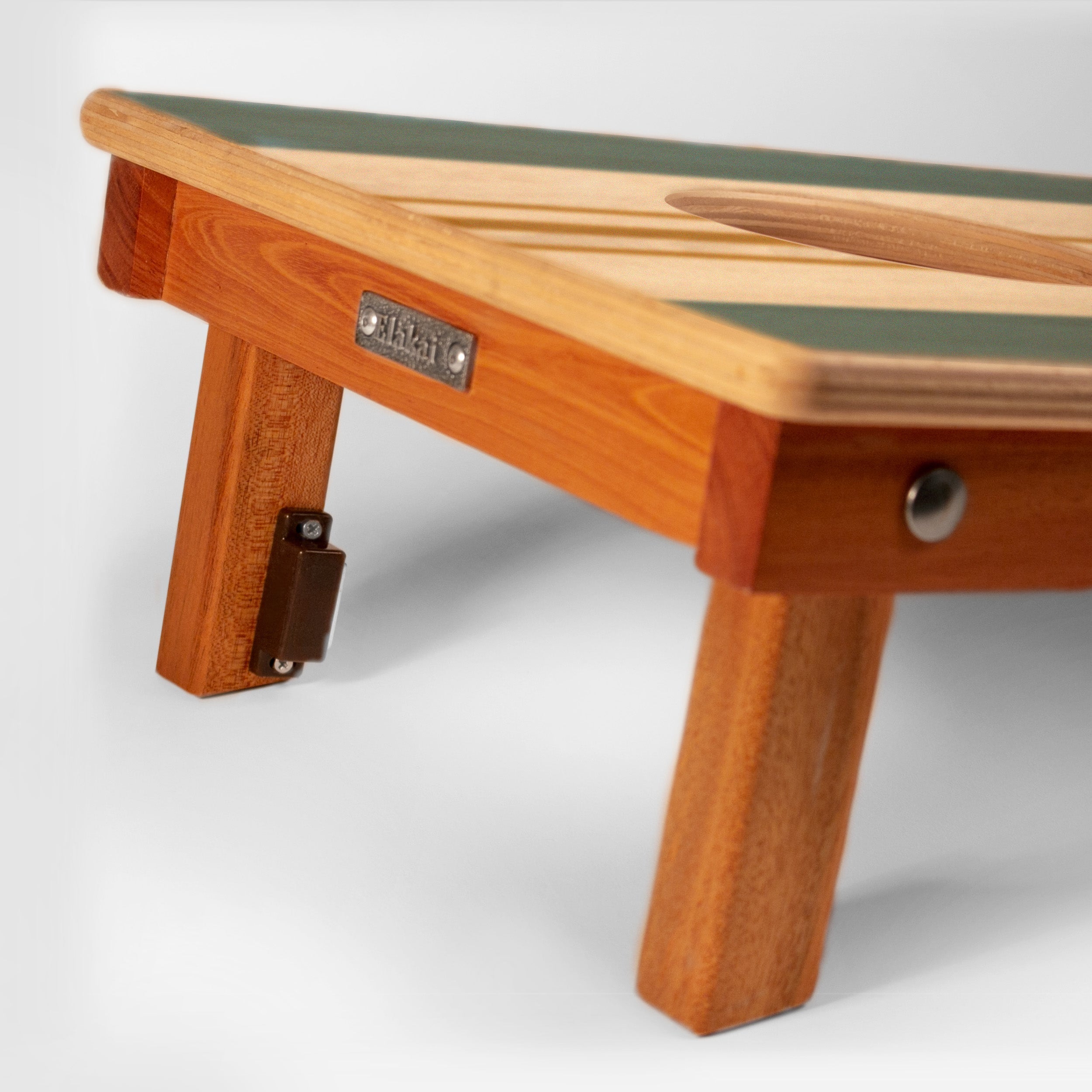 Close-up of a wooden folding table with a warm honey-toned wood frame, a green top edge, and a metal brand plate reading 'STUDY'.