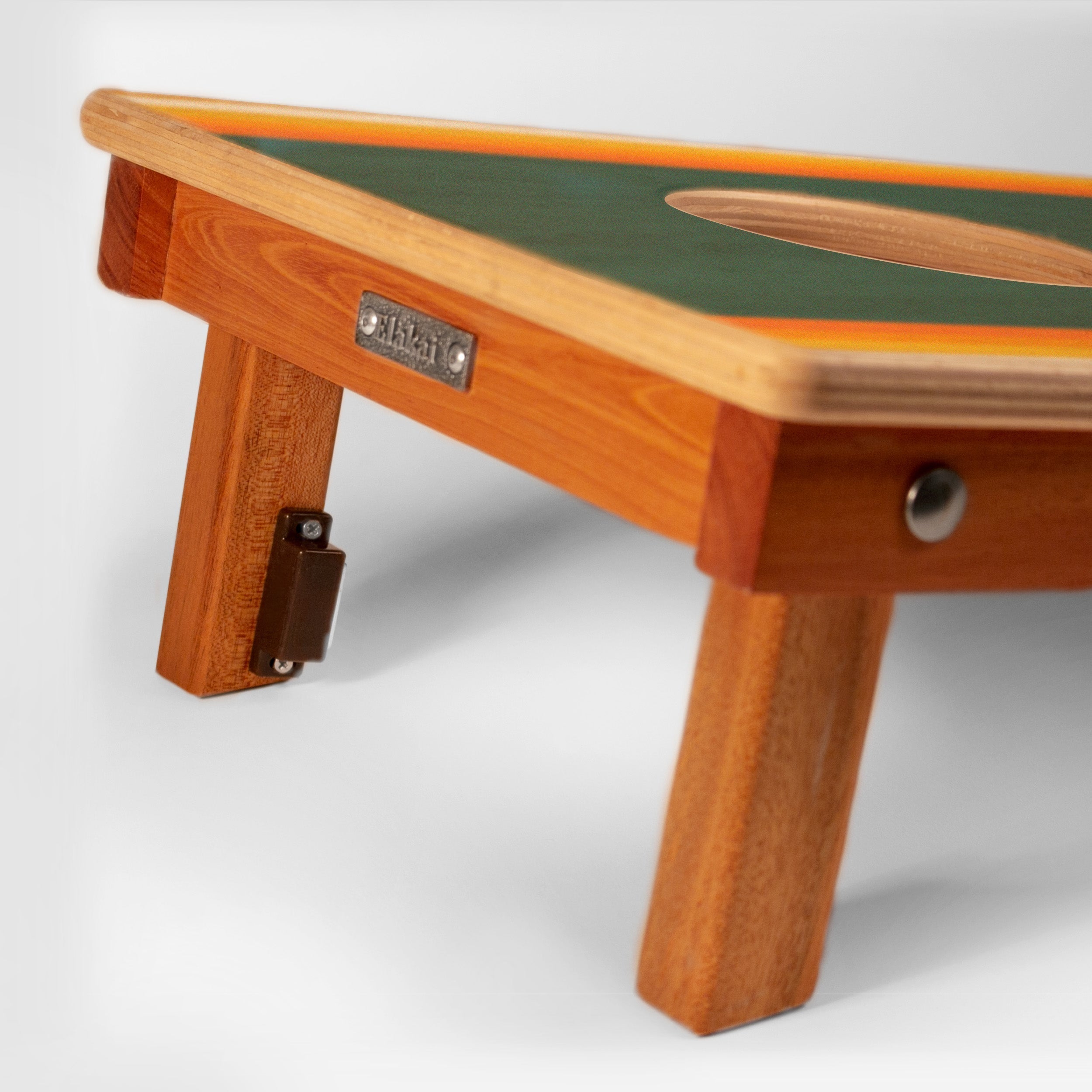 Close-up of a folding wooden table with a green top, orange trim, and light wood legs, shown on a light gray studio background.