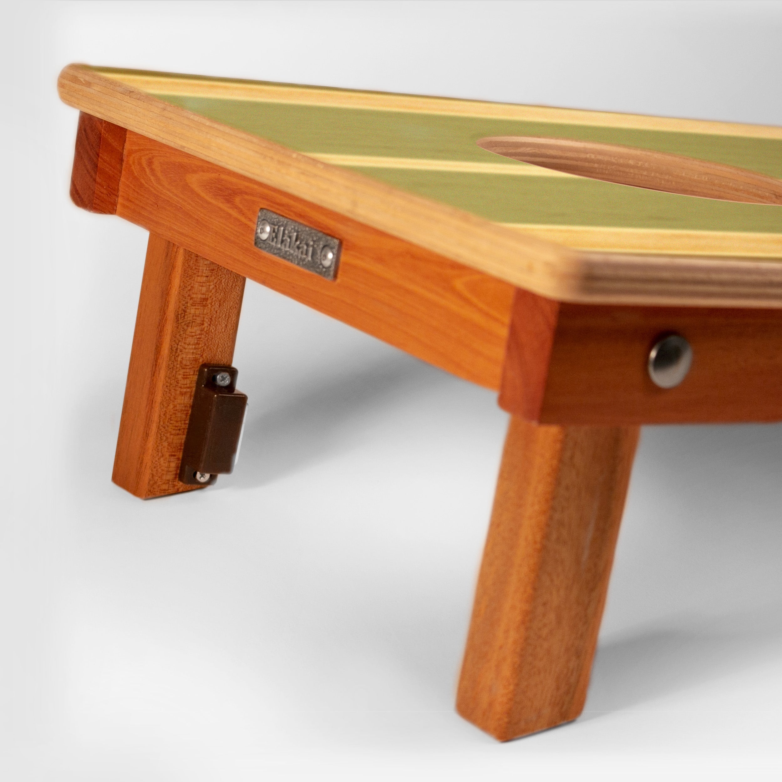 Close-up of a wooden folding table with a light green and beige striped top, warm brown wood frame, and metal hardware, shown on a light gray studio background.