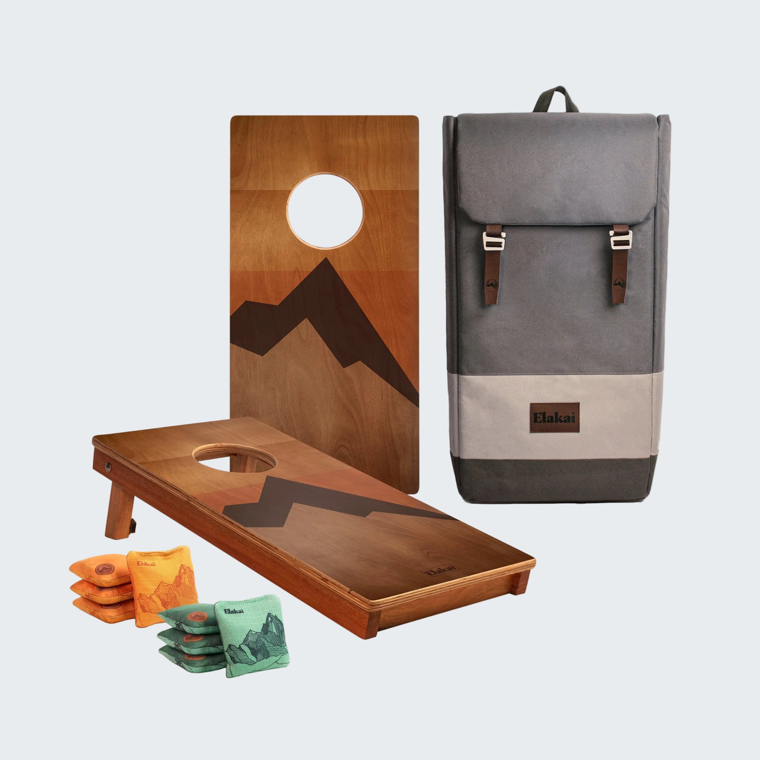 Cornhole boards with mountain design, bags, and a gray backpack on a white background