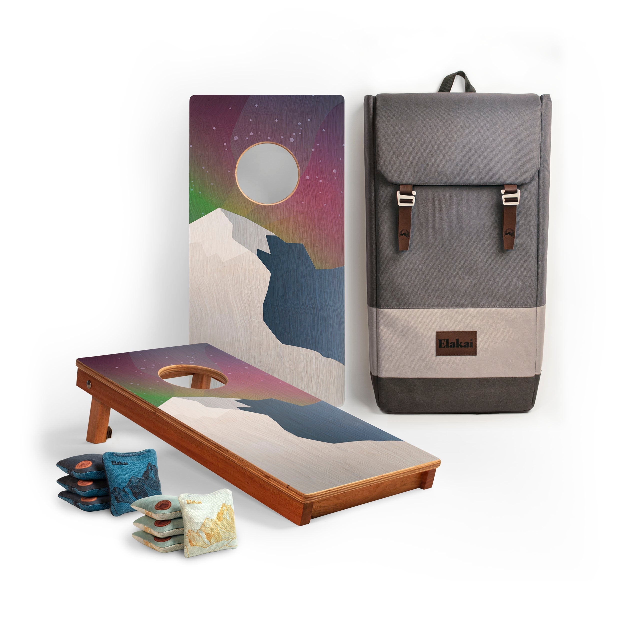 Cornhole boards with mountain design, cornhole bags, and a gray backpack on a white background
