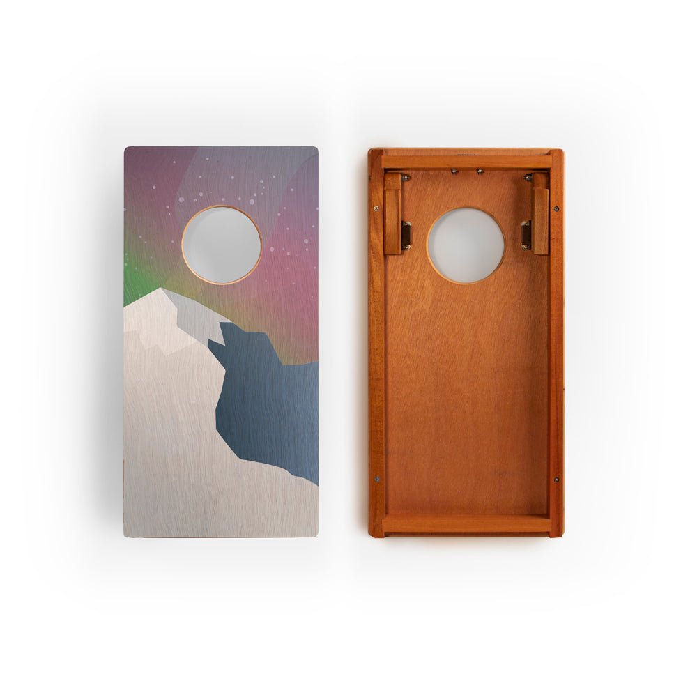 Two wooden bean bag toss boards with one featuring a colorful abstract design and the other a plain brown surface.