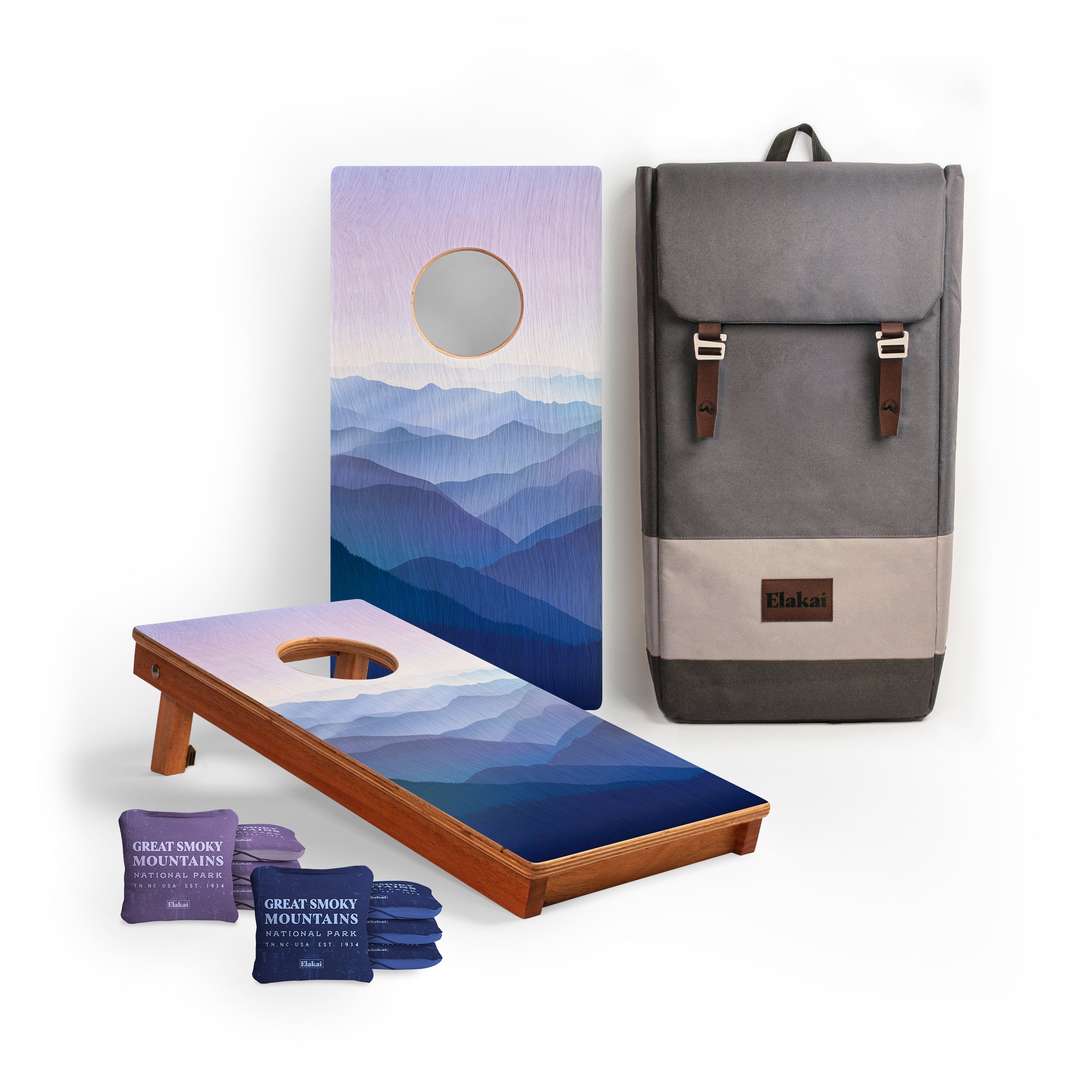 Cornhole board with mountain design, cornhole bags, and a backpack on a white background