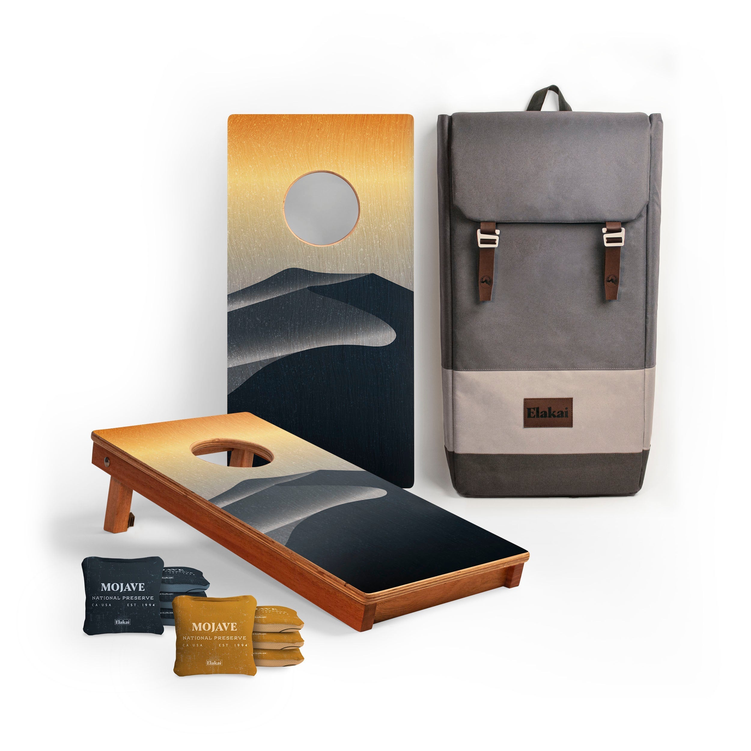 Cornhole board with mountain design, gray backpack, and bean bags on a white background