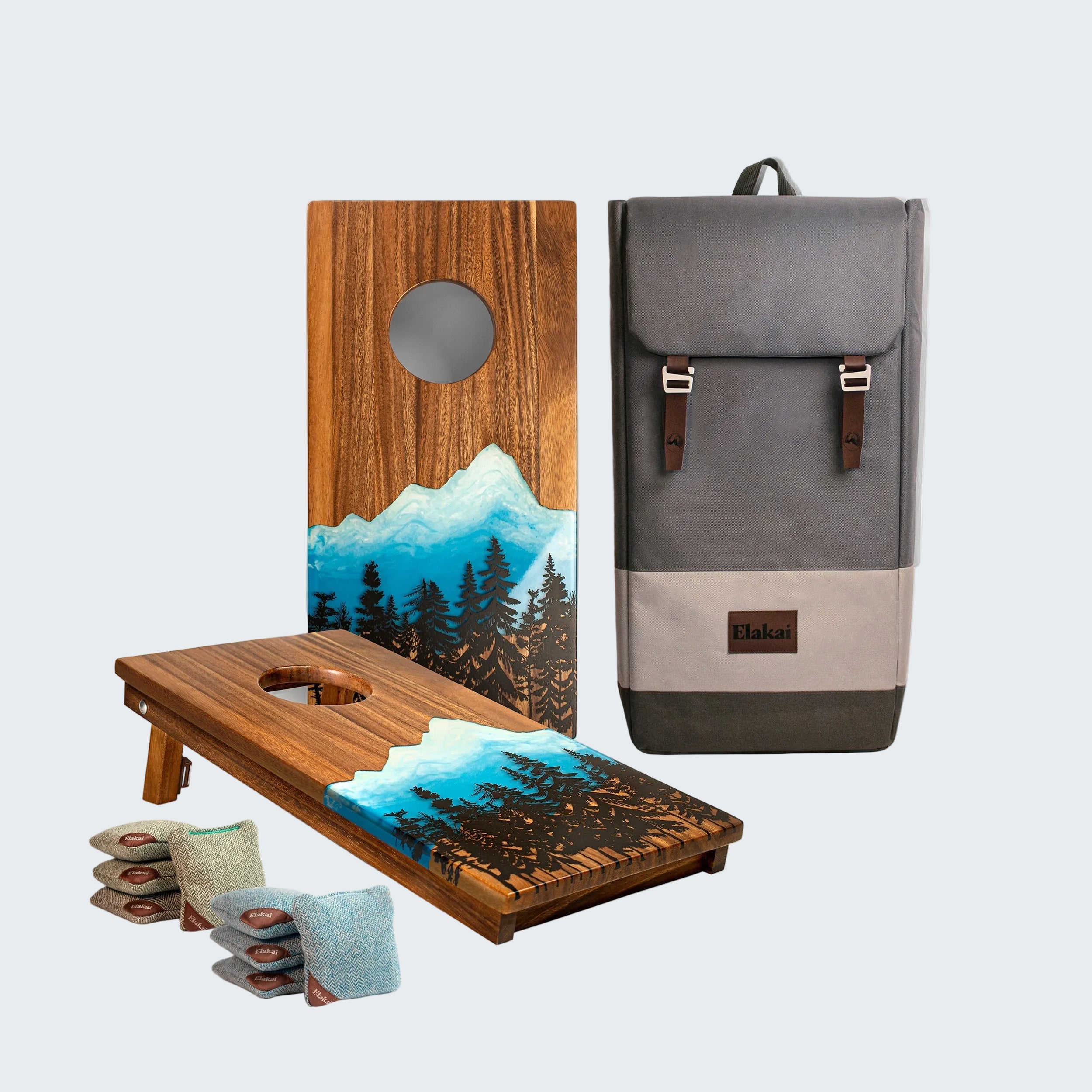Wooden cornhole boards with mountain design and a gray backpack on a white background