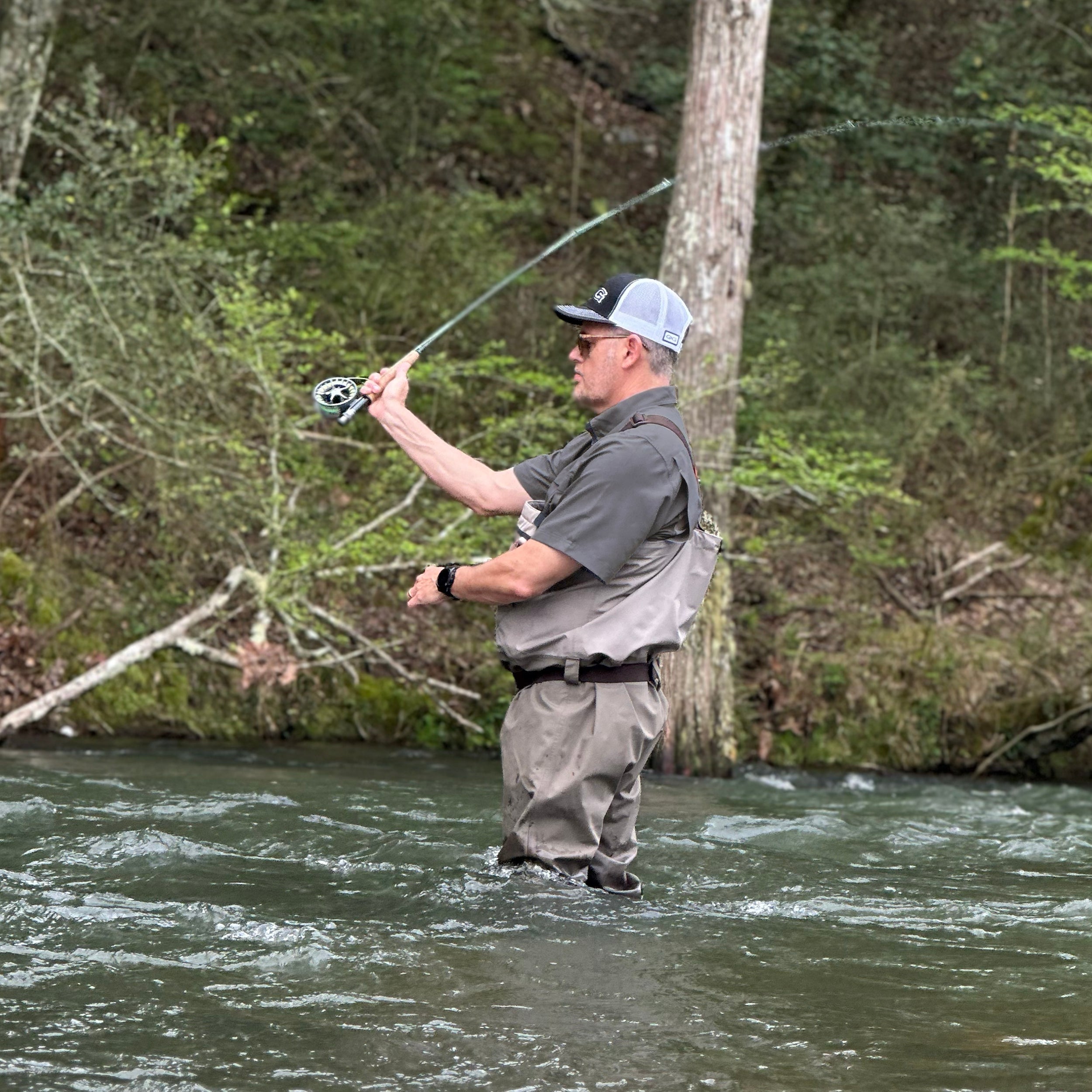 Man fishing in a river surrounded by trees