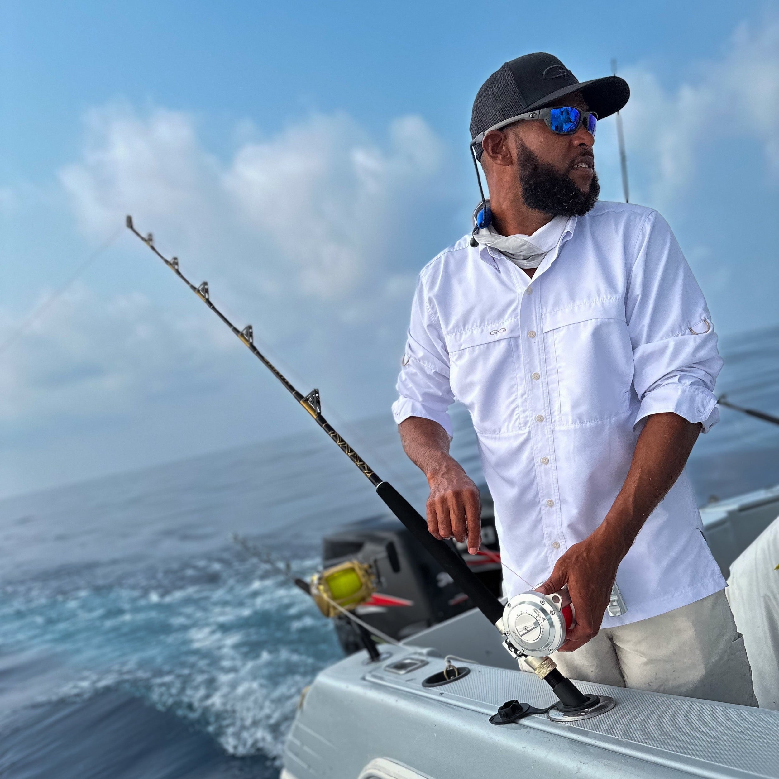Man on a boat holding a fishing rod with a clear sky and ocean background