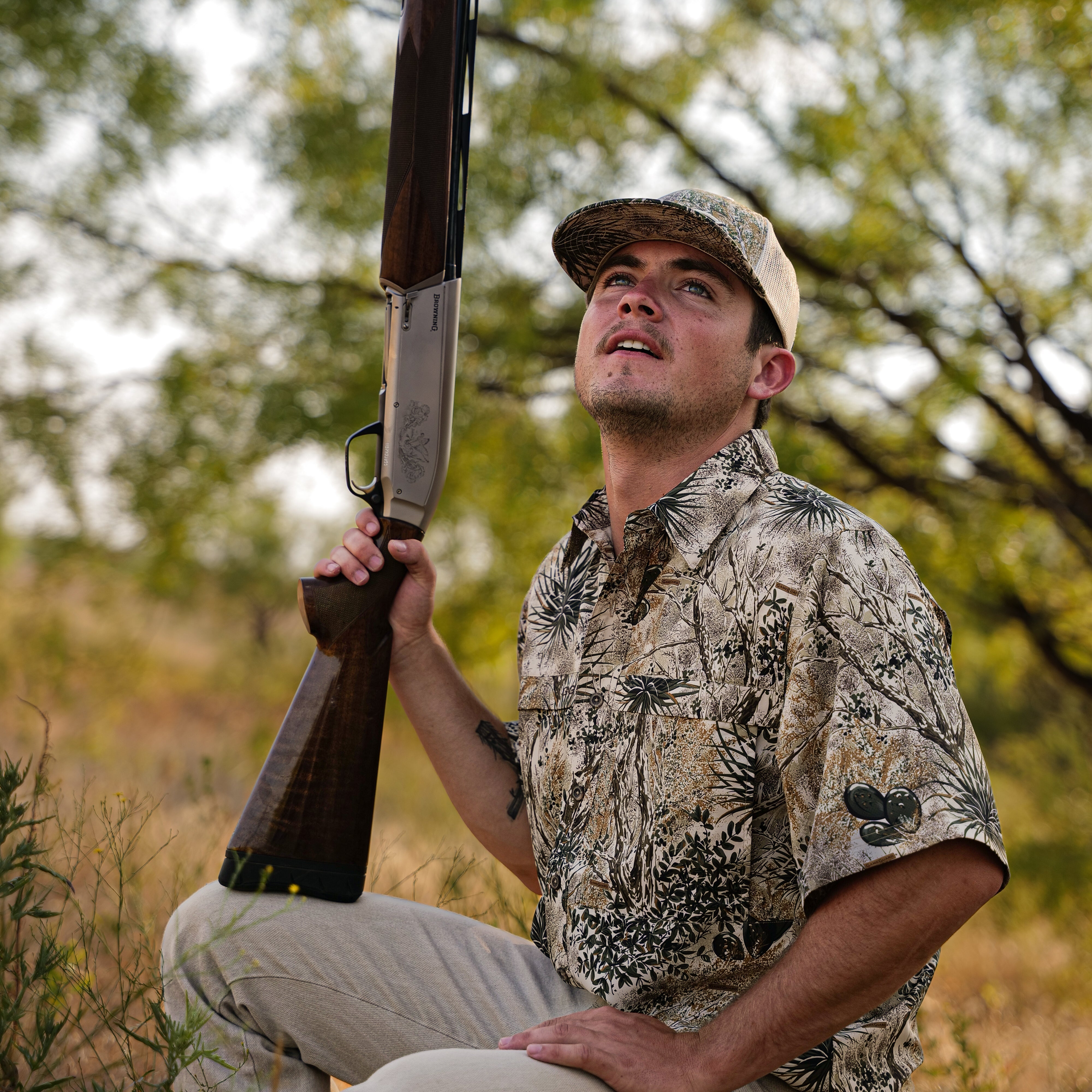 Man in camouflage shirt and cap holding a rifle in a natural setting