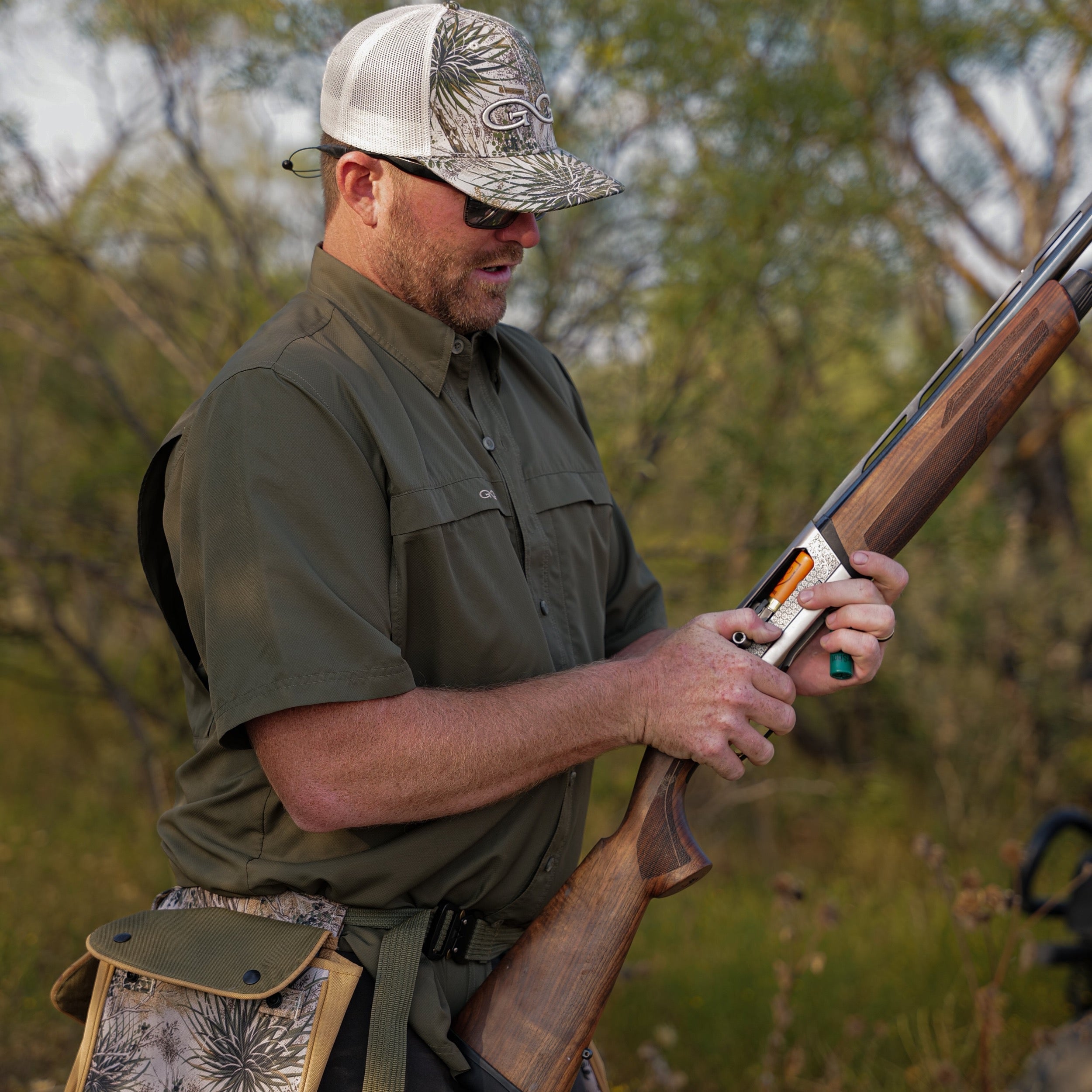 Man in hunting attire holding a rifle in a natural setting
