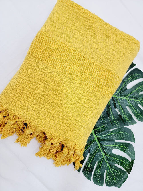 Yellow towel with fringes on a white background with a green leaf