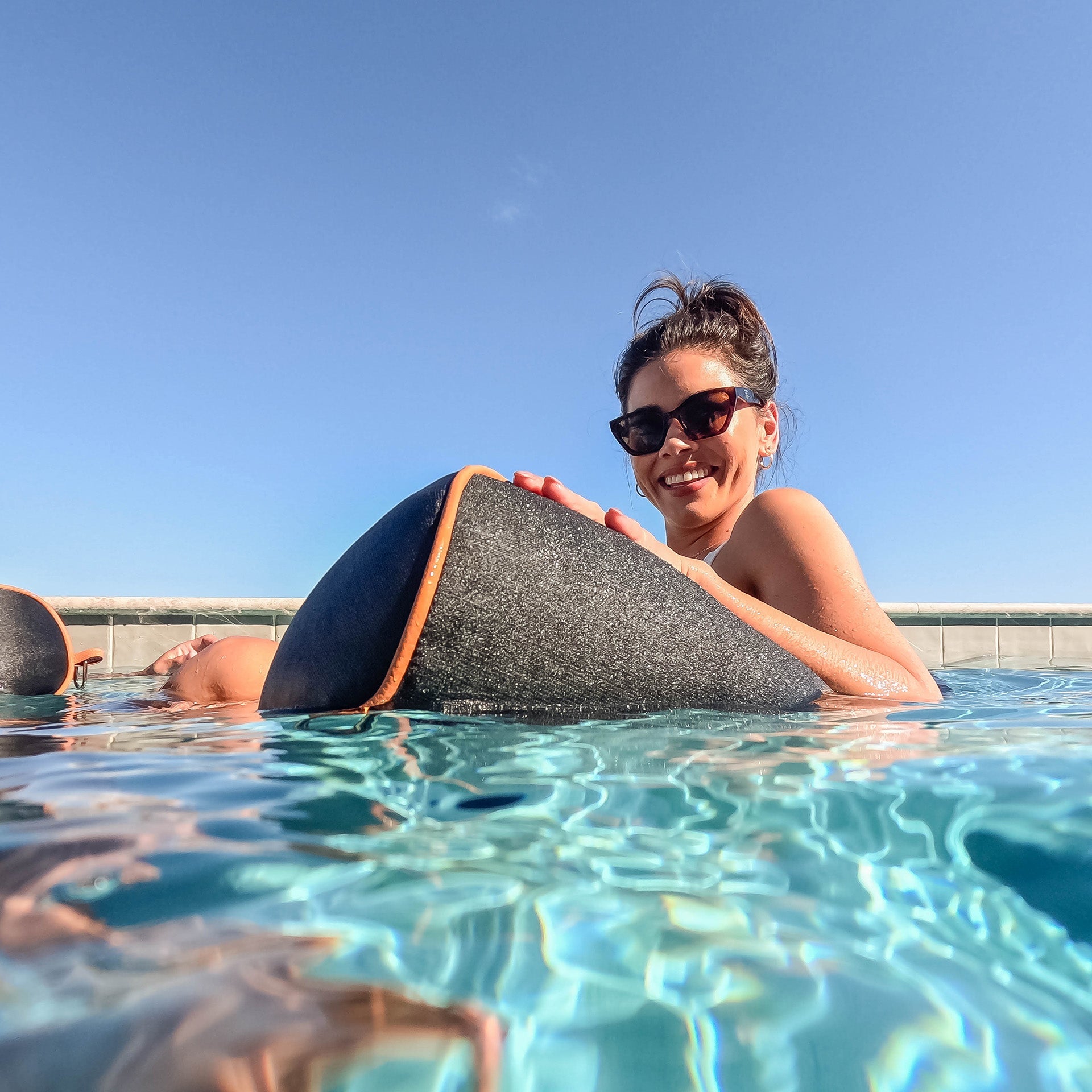 Person holding a triangular object in a pool with a clear blue sky.