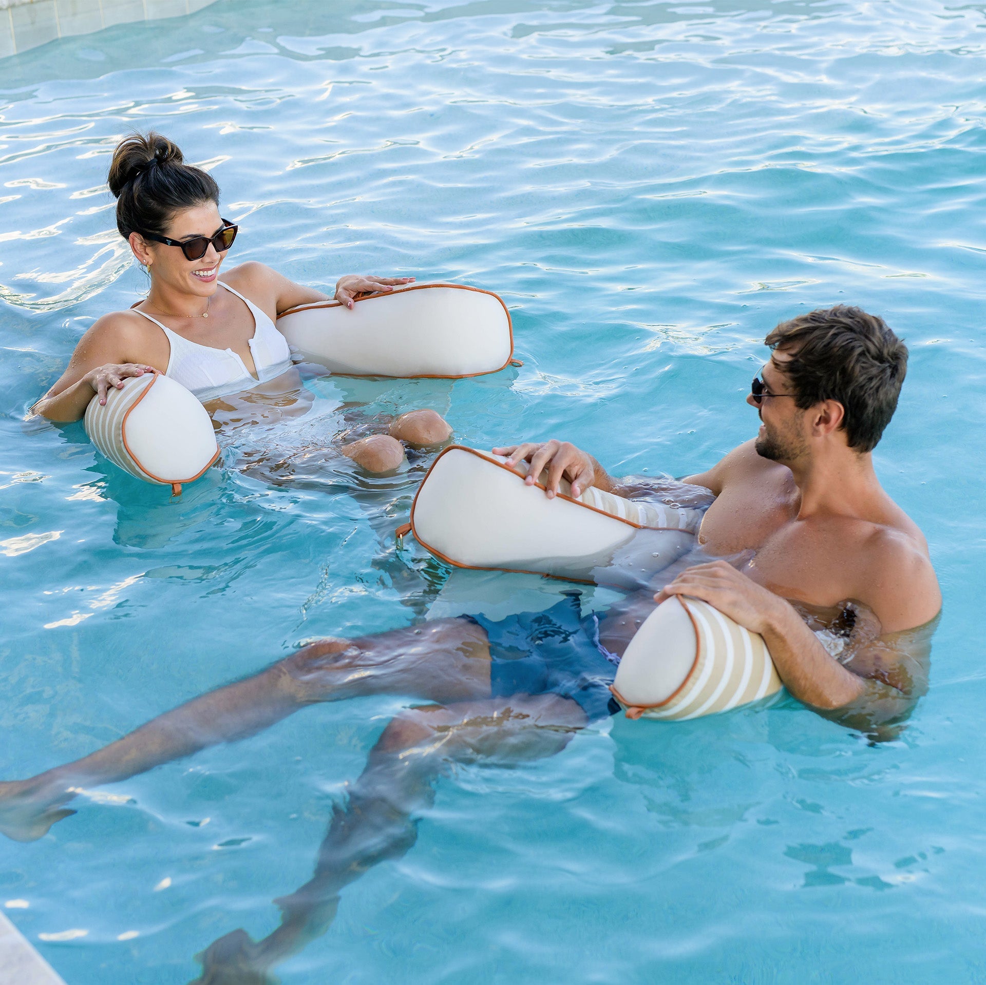 Two people in a pool using inflatable rings.
