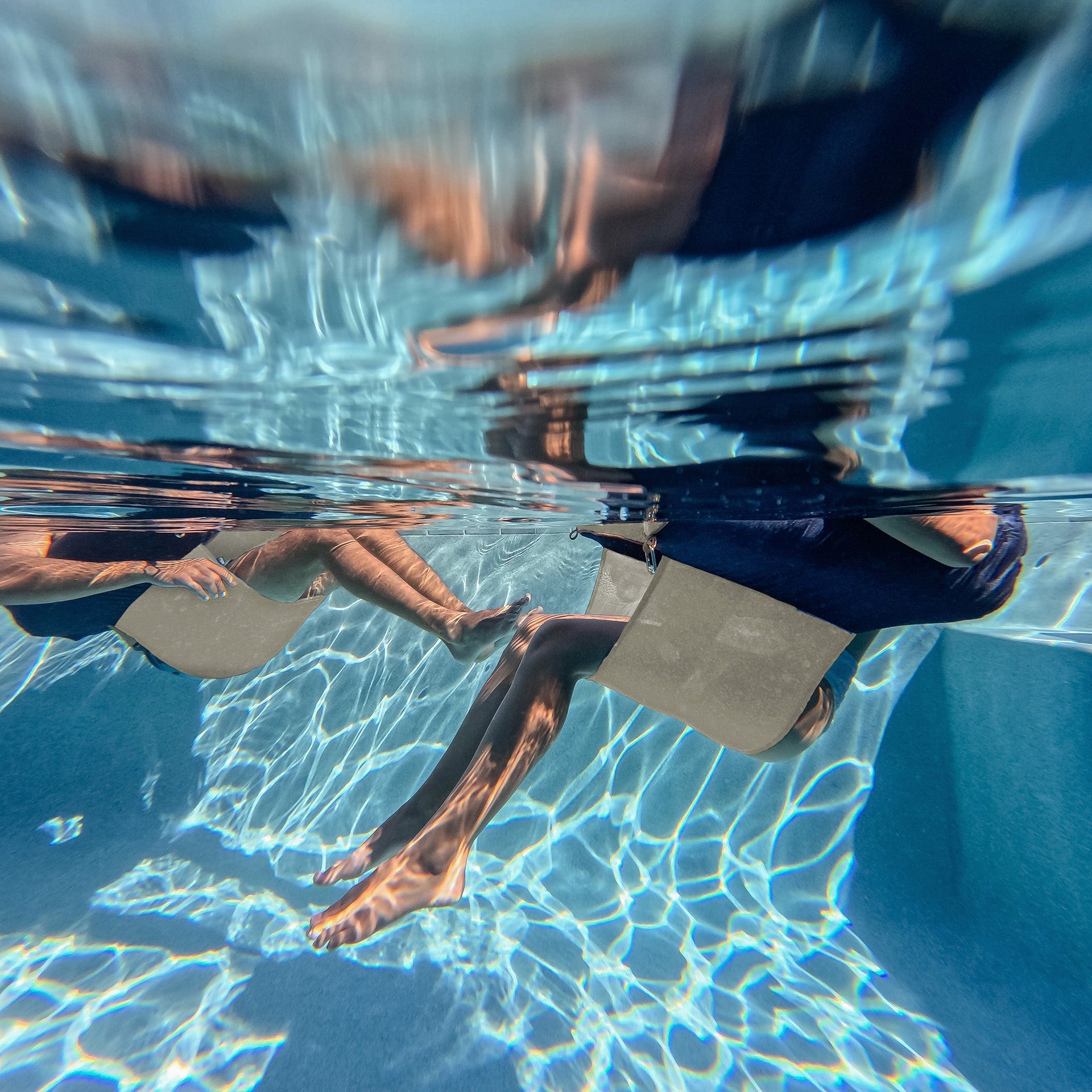 Underwater view of a person sitting with feet visible, holding hands with another person.