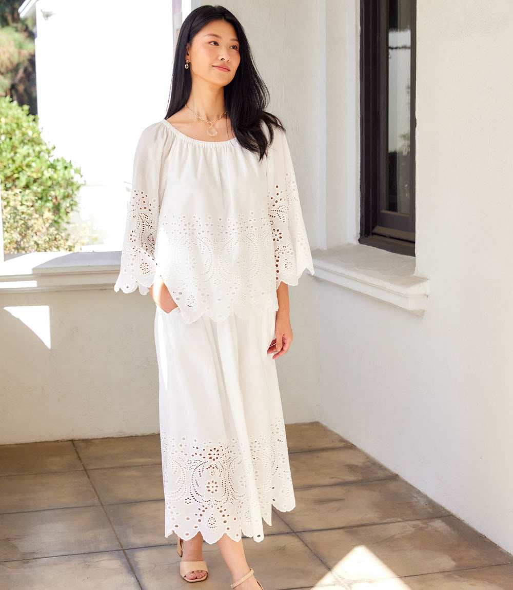 Woman wearing a white dress with lace details standing on a patio.
