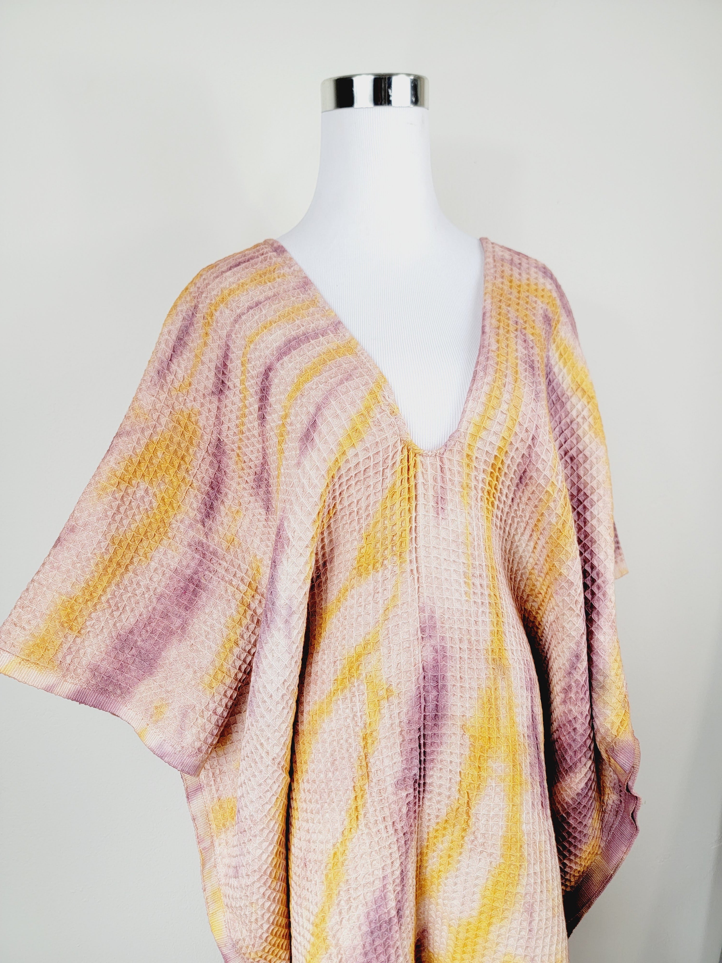 Mannequin wearing a pink and yellow patterned poncho against a white background