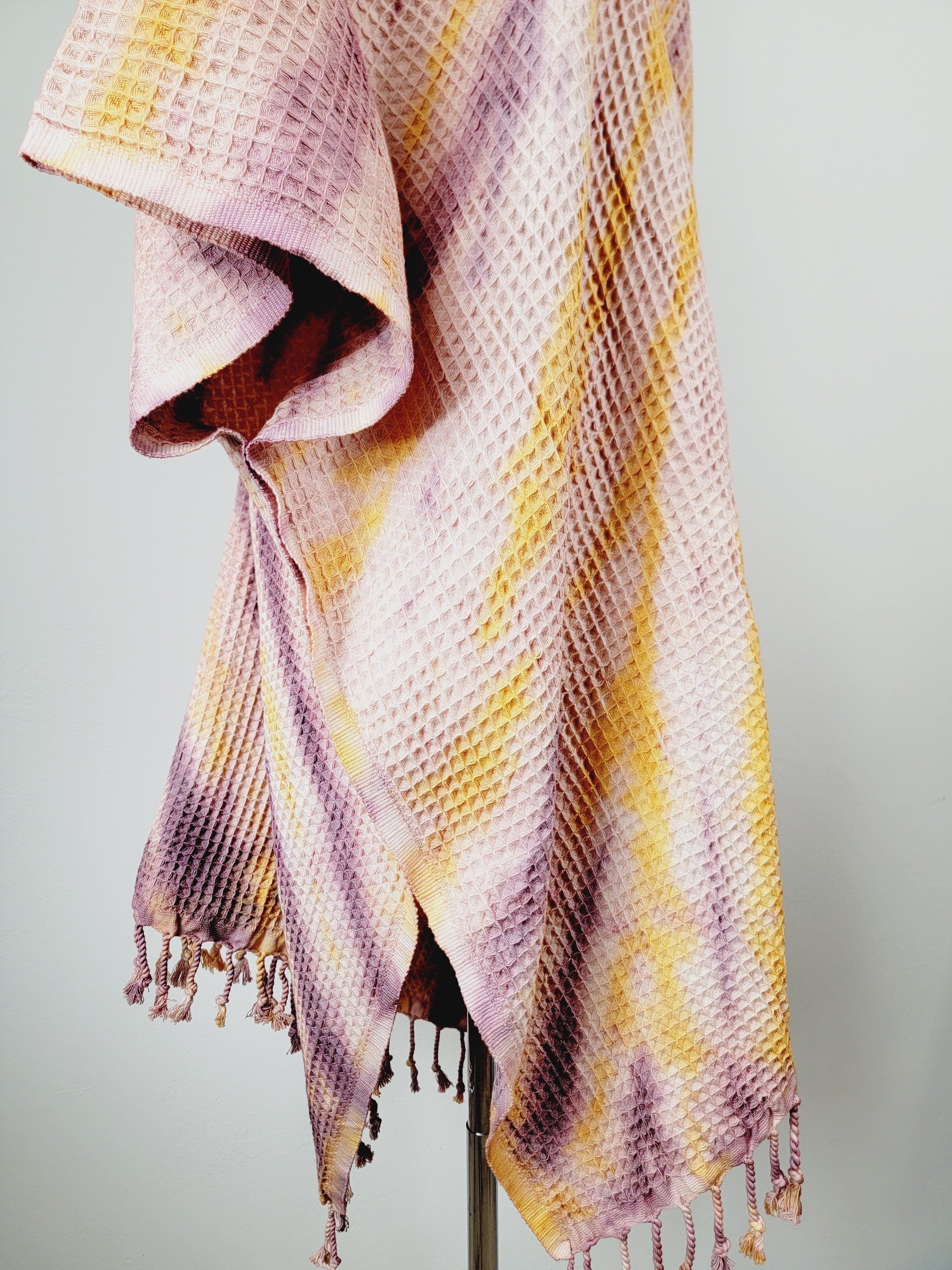 Woven blanket with purple and yellow stripes on a stand against a gray background