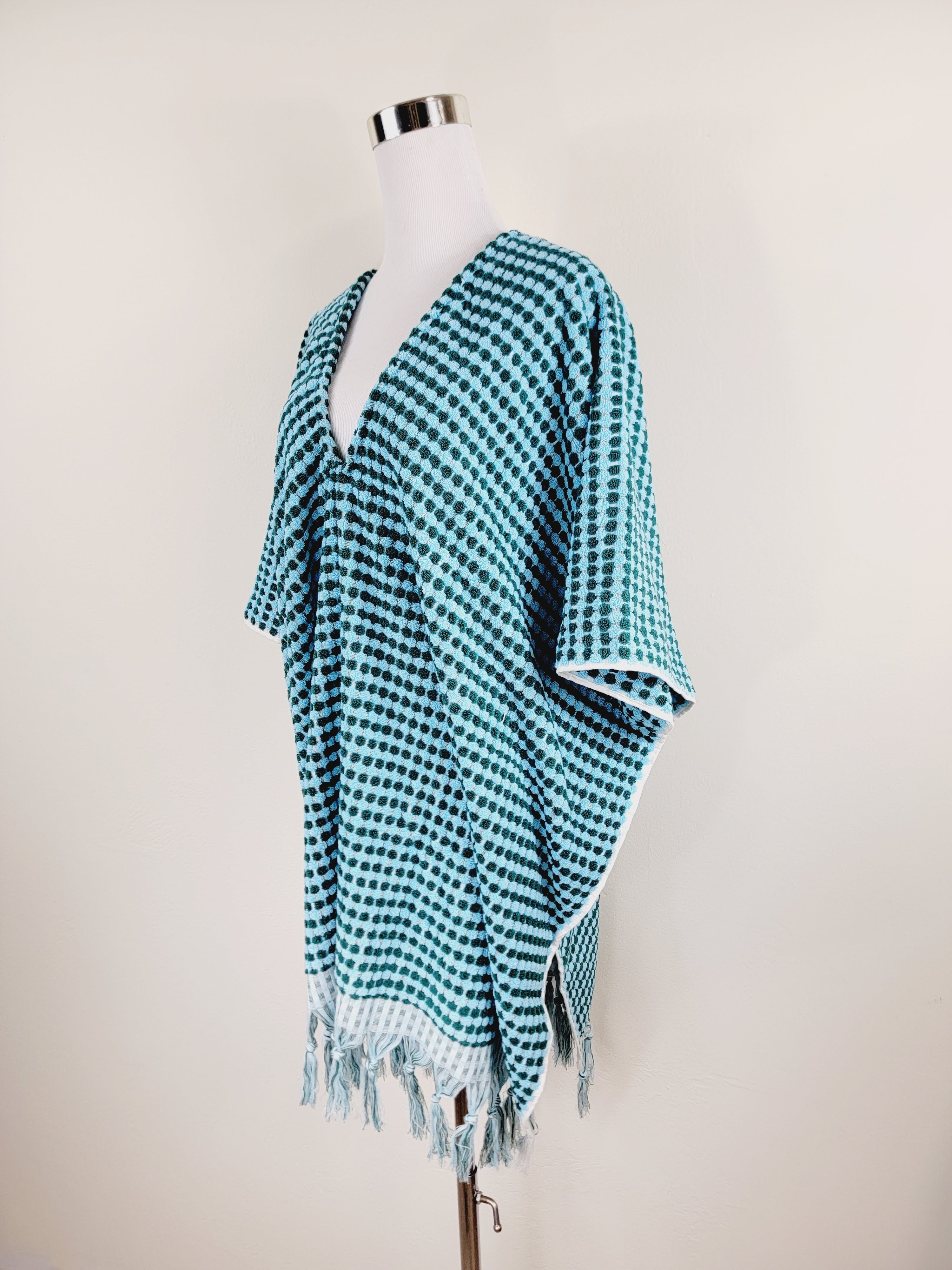 Mannequin wearing a turquoise and white checkered shawl with fringes on a plain background