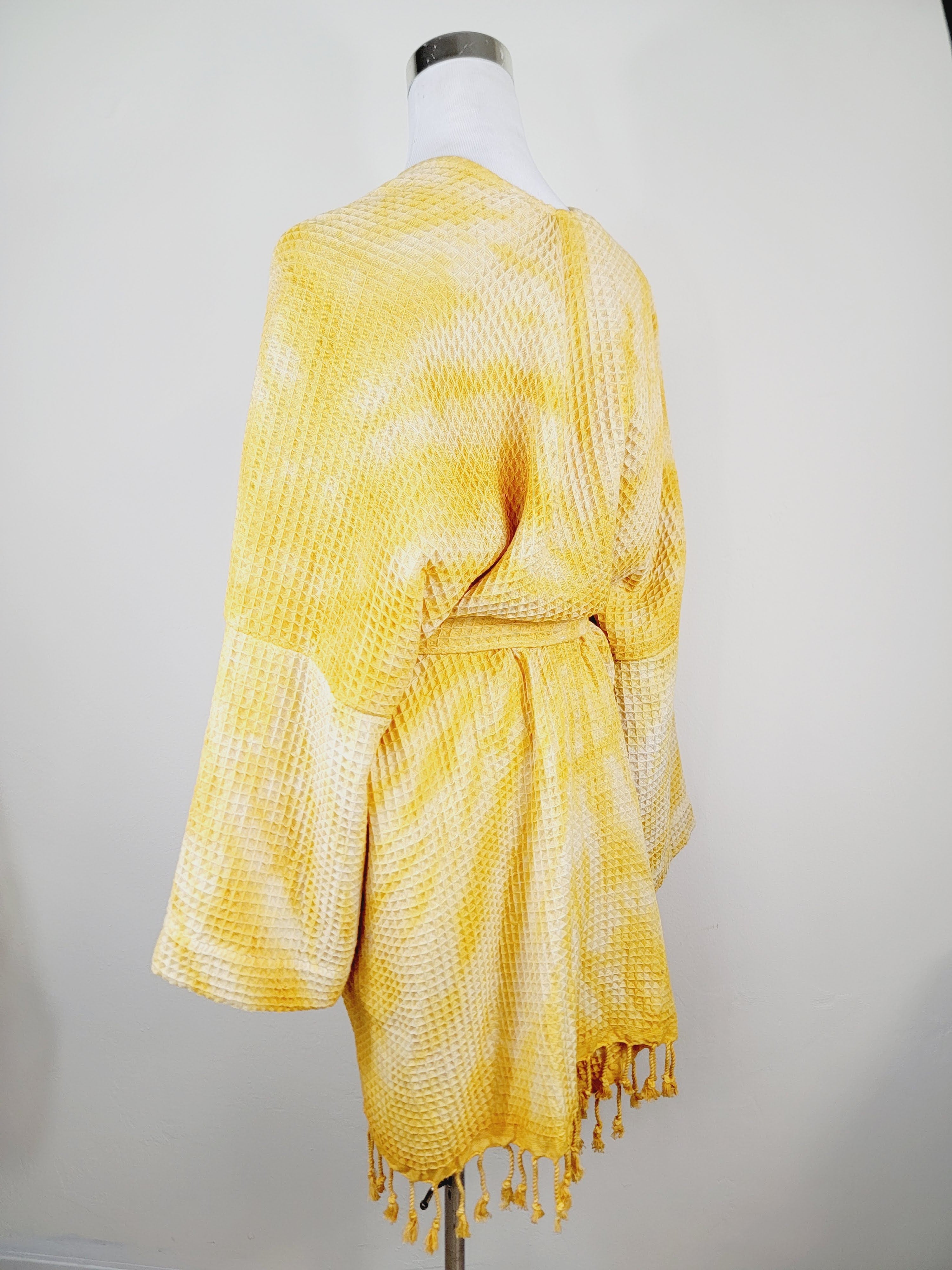 Yellow tie-dye dress with fringes on a mannequin against a plain background