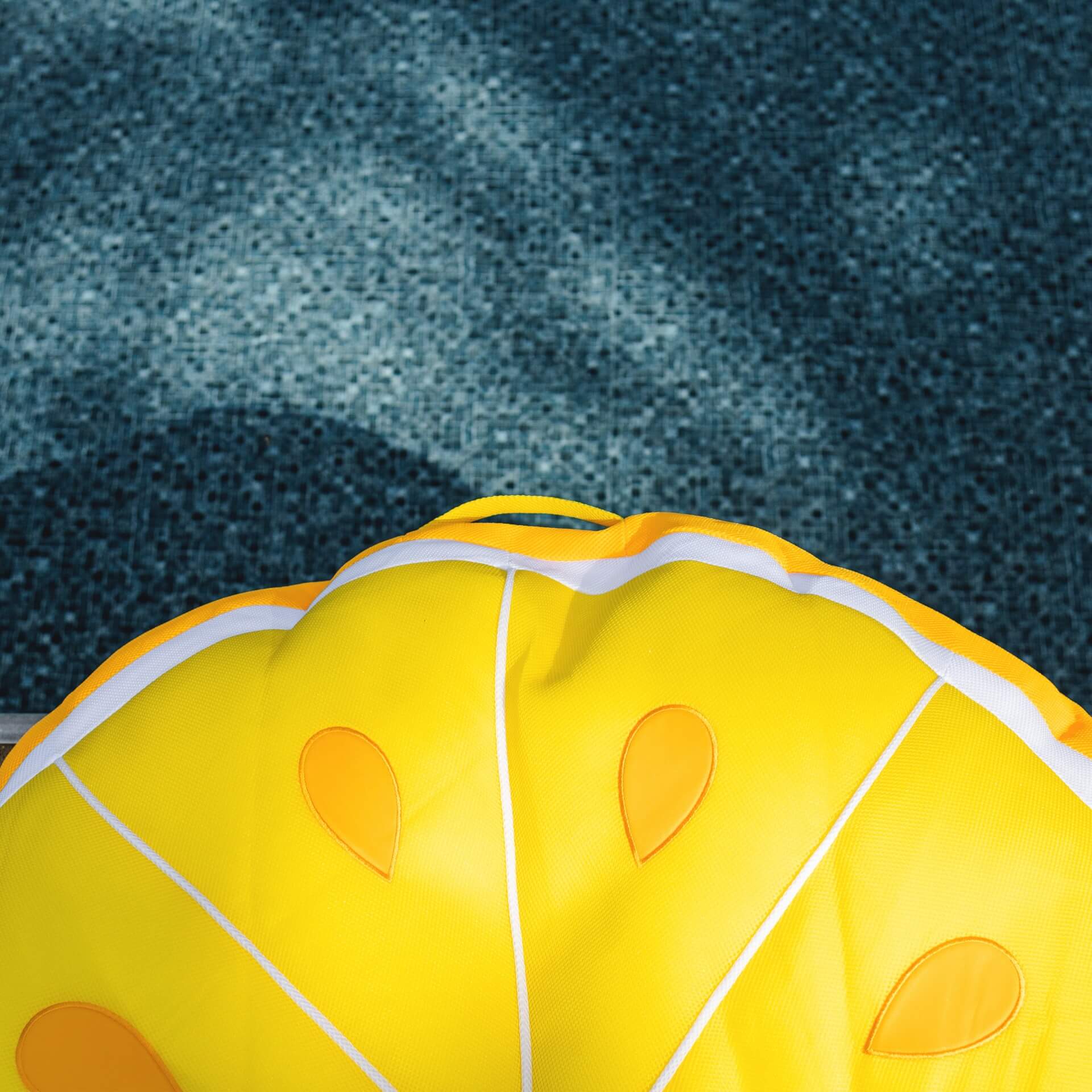 Yellow inflatable pool toy with orange spots on a textured blue background
