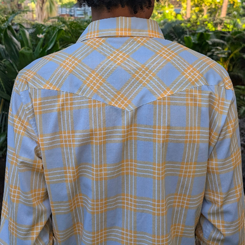 Person wearing a blue and yellow plaid shirt with a blurred natural background