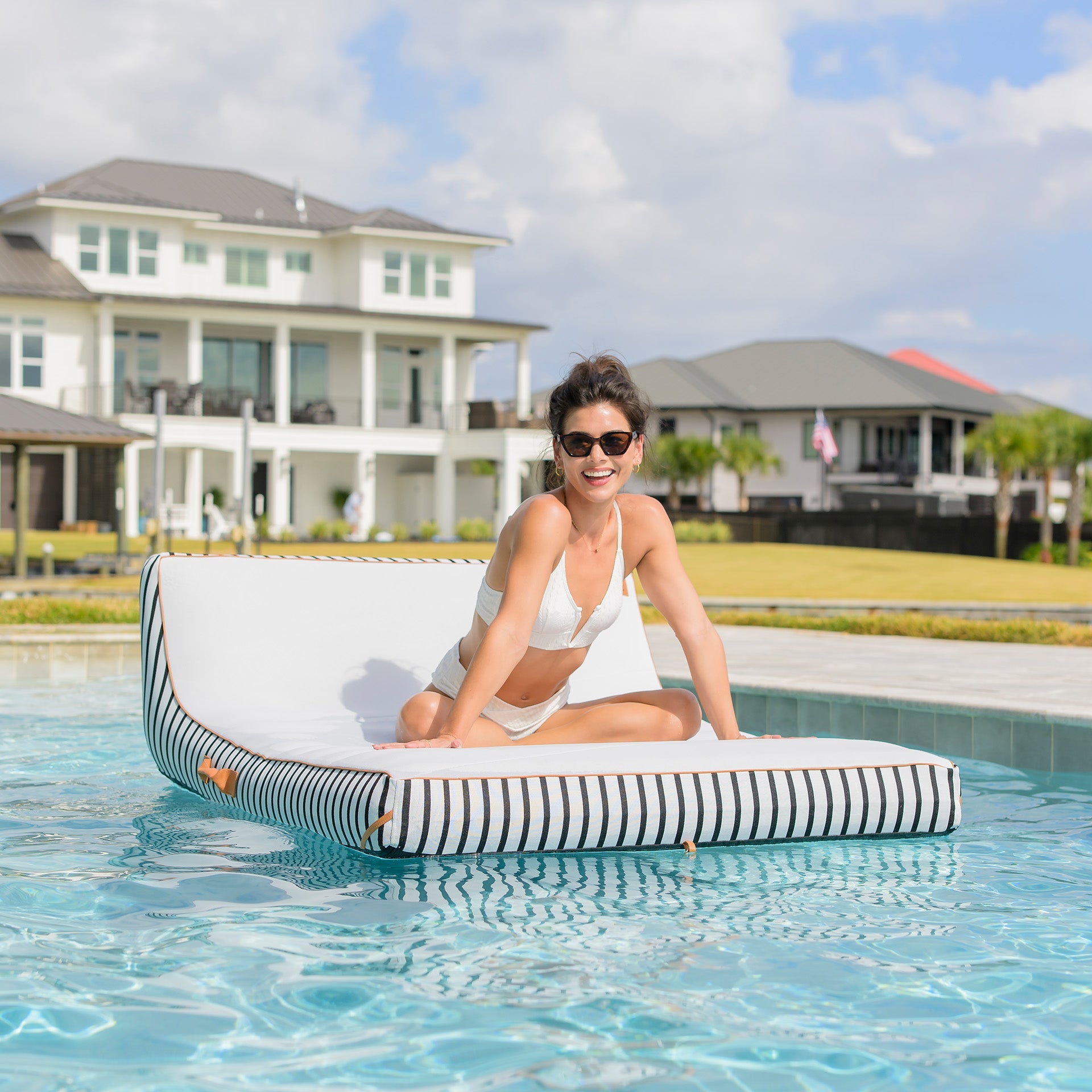 Woman sitting on a striped pool float in a swimming pool with a house in the background