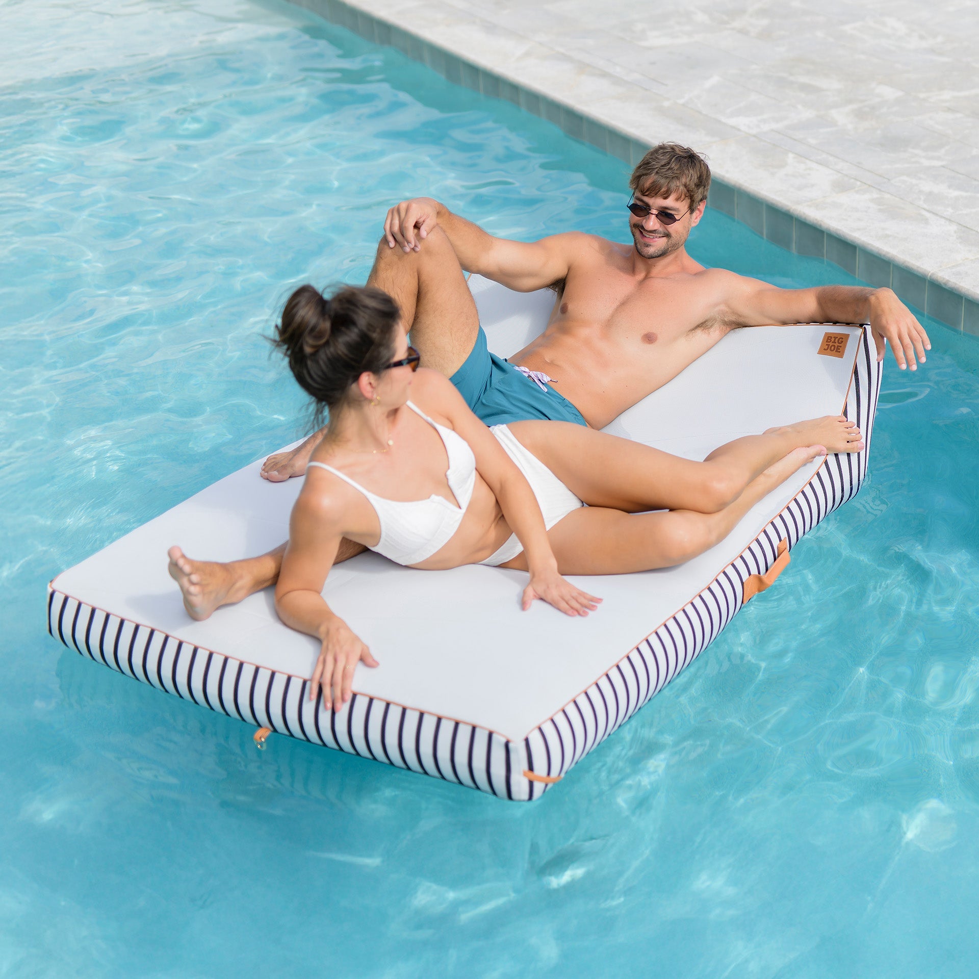 Two people relaxing on a floating inflatable platform in a pool.