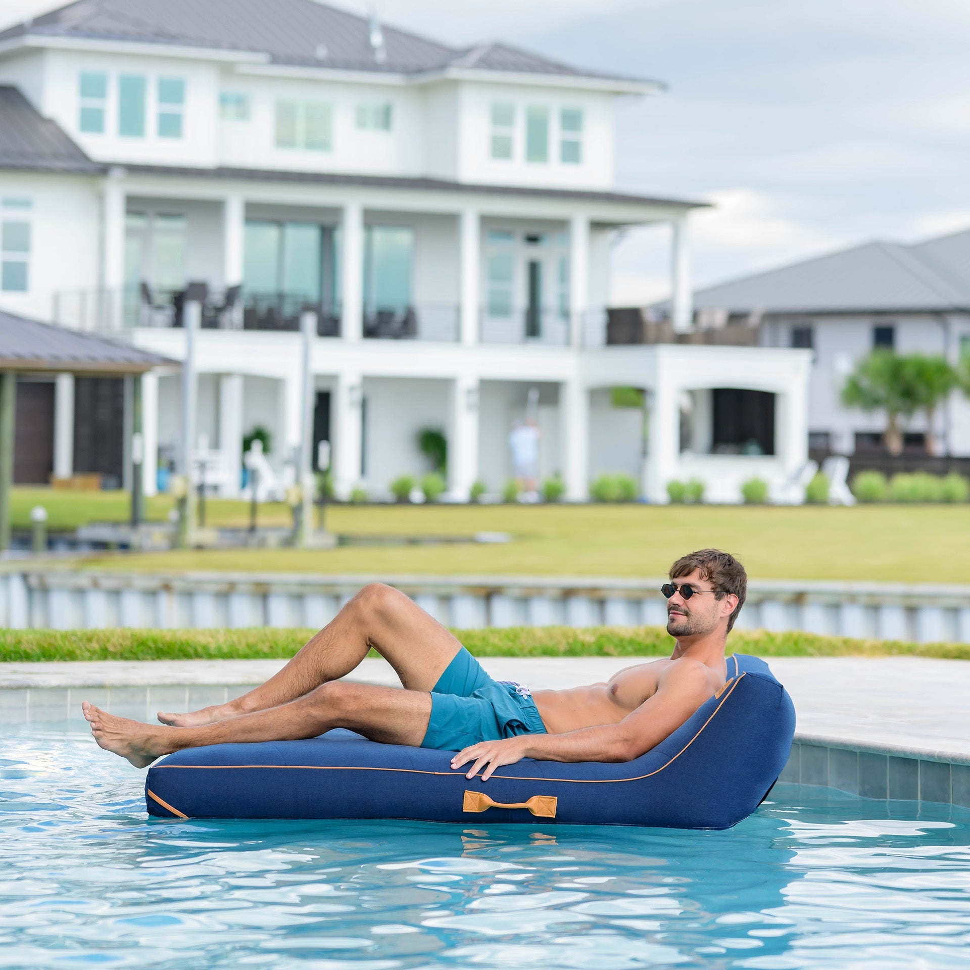 Man lounging on an inflatable pool float in a swimming pool with a house in the background