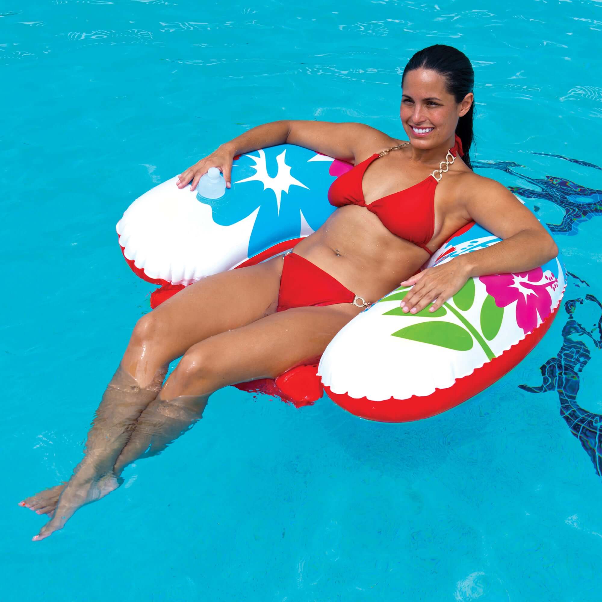 Woman in a red bikini sitting on a floral-patterned inflatable ring in a pool.