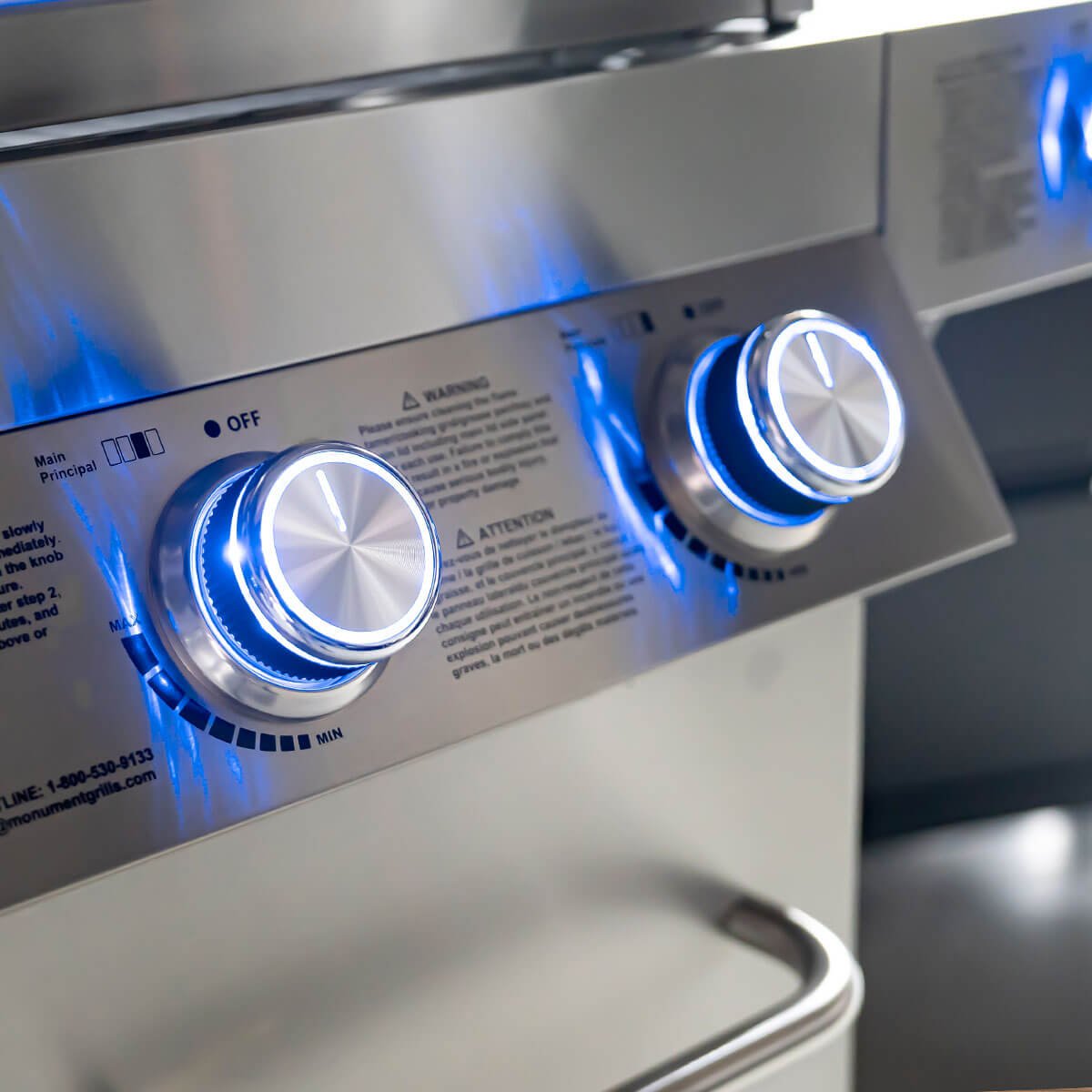 Close-up of a stainless steel grill with control knobs and blue flames.